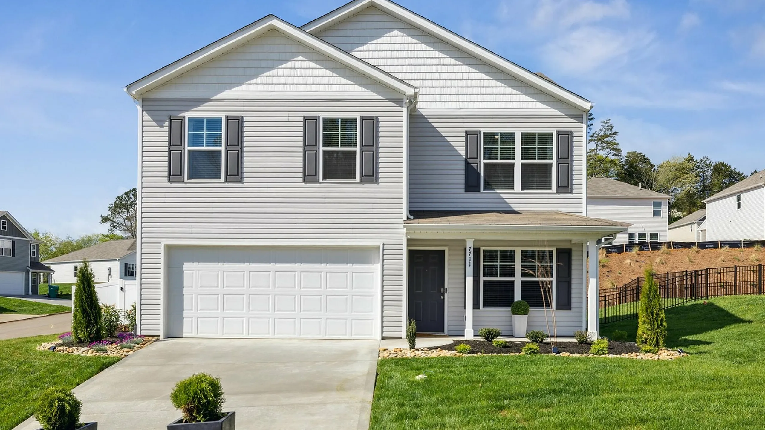 Inviting modern two-story home featuring a two-car garage, charming front porch, and lush landscaping, bathed in bright natural light.