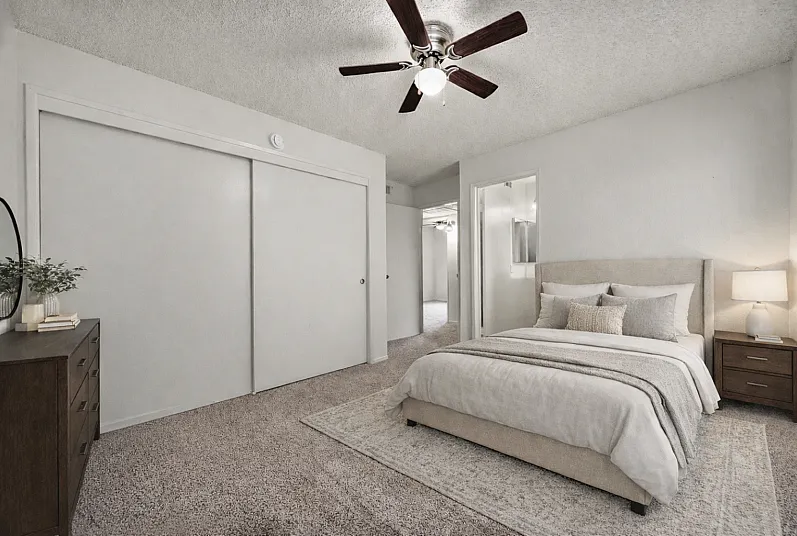Spacious primary bedroom with neutral tones, carpet flooring, ceiling fan, and sliding closet doors