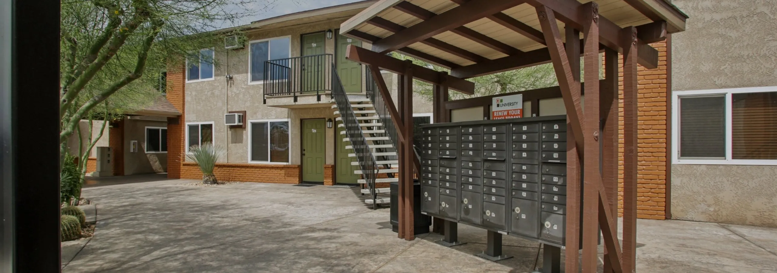 Charming apartment exterior with modern mailboxes, green doors, and inviting upper-level balconies, surrounded by lush greenery.