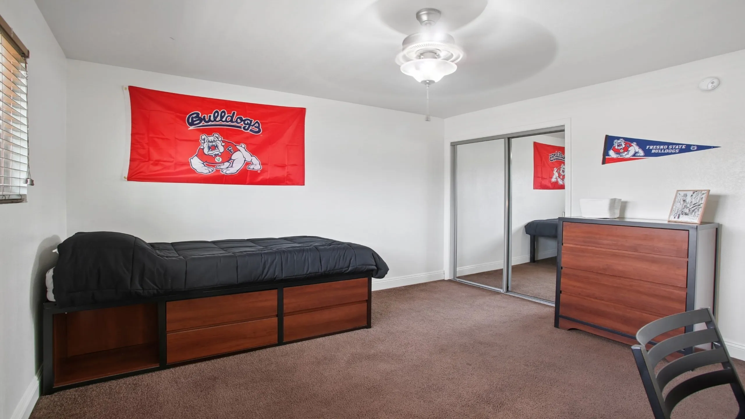 Bright bedroom featuring a cozy single bed, mirrored closet, and desk with Fresno State decor.