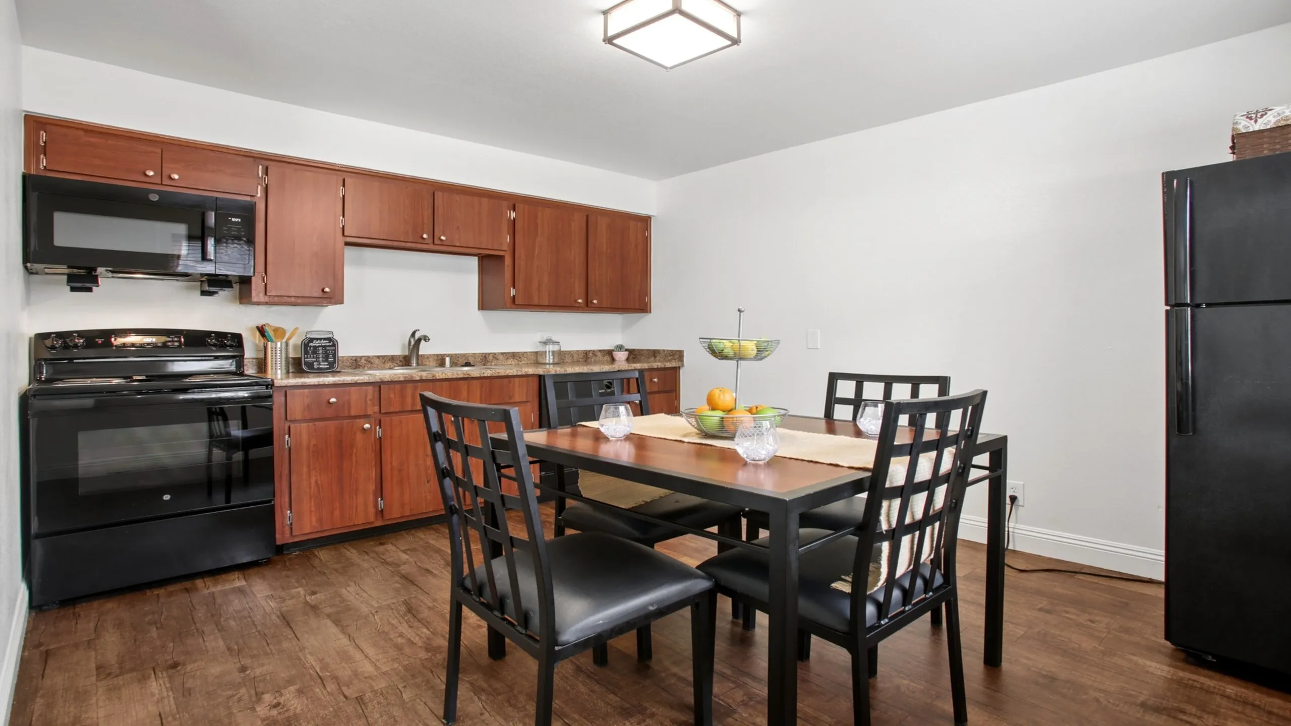 Modern kitchen and dining area featuring sleek black appliances, elegant wooden cabinetry, and a cozy dining table set for four.