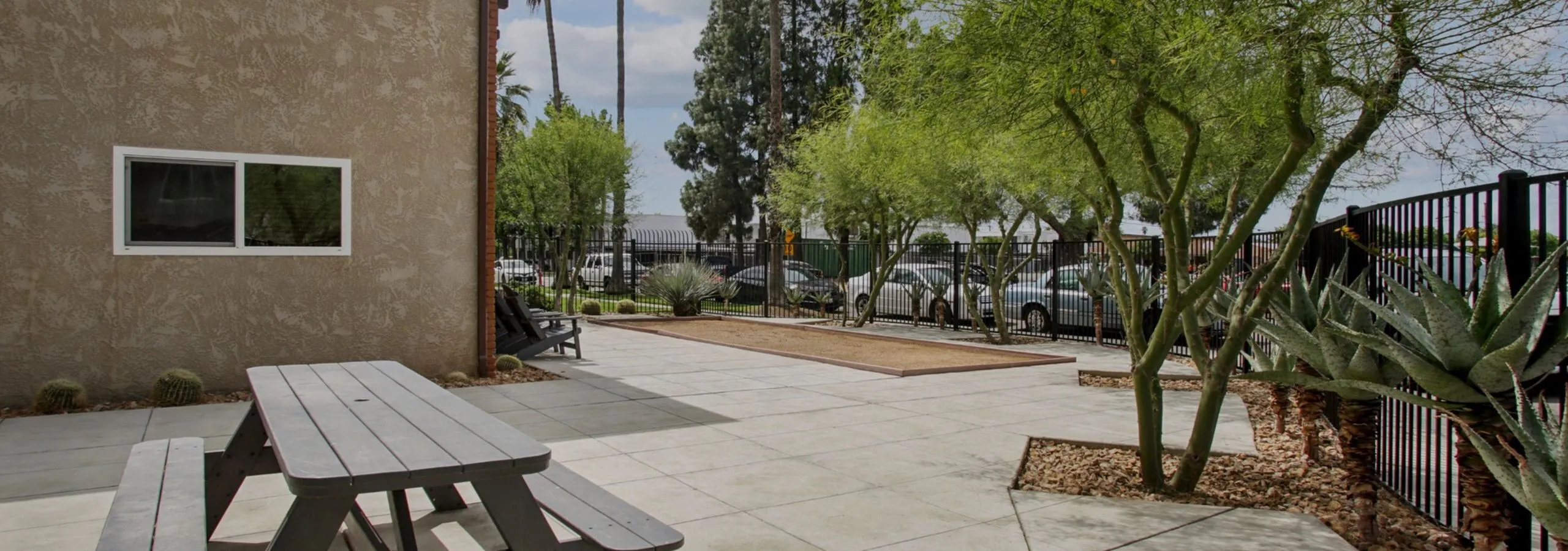 Charming outdoor patio with picnic table, lush trees, and modern fence, perfect for relaxation and entertainment.