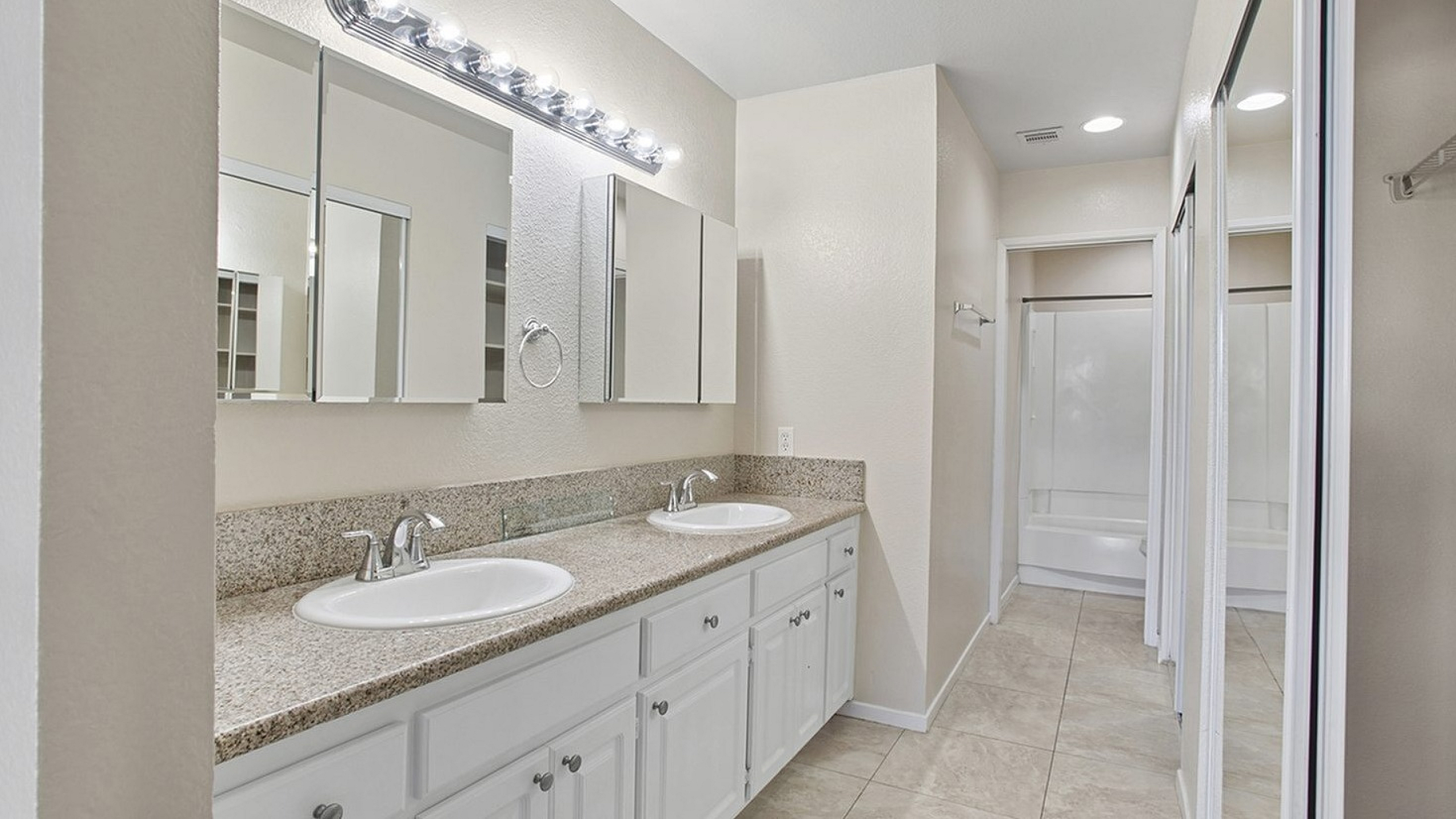Elegant bathroom with dual sinks, sleek granite countertops, and ample cabinet storage beneath bright, modern lighting.
