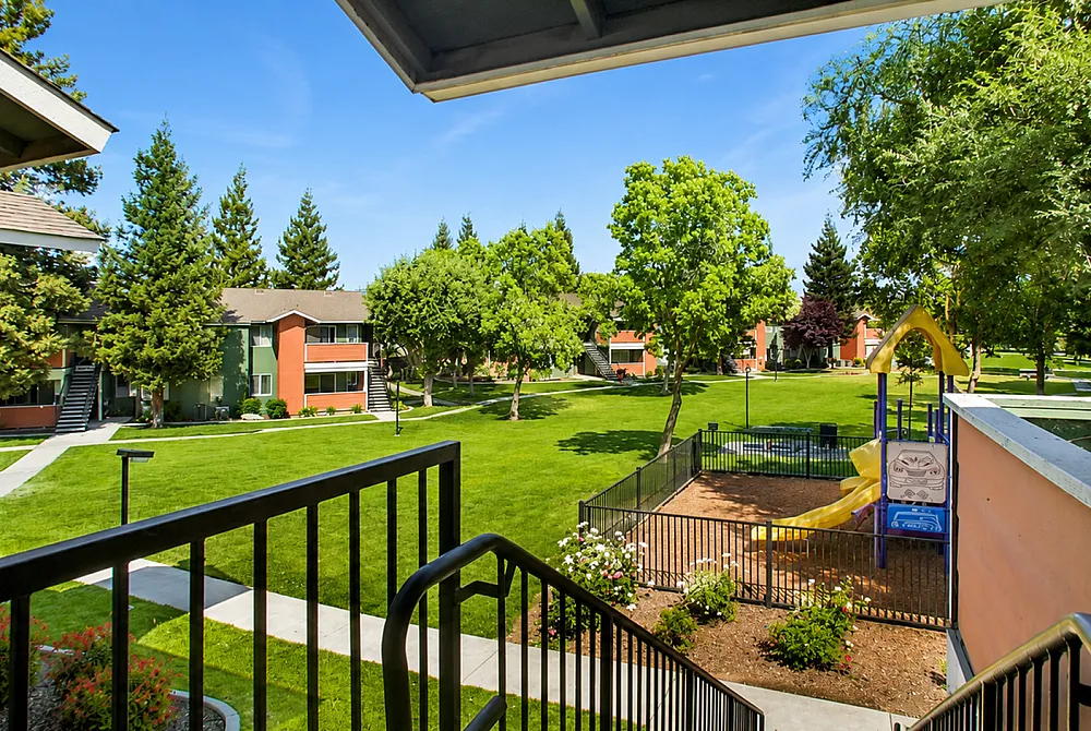 Charming residential community view with lush green lawns, mature trees, and children's playground under a clear blue sky.