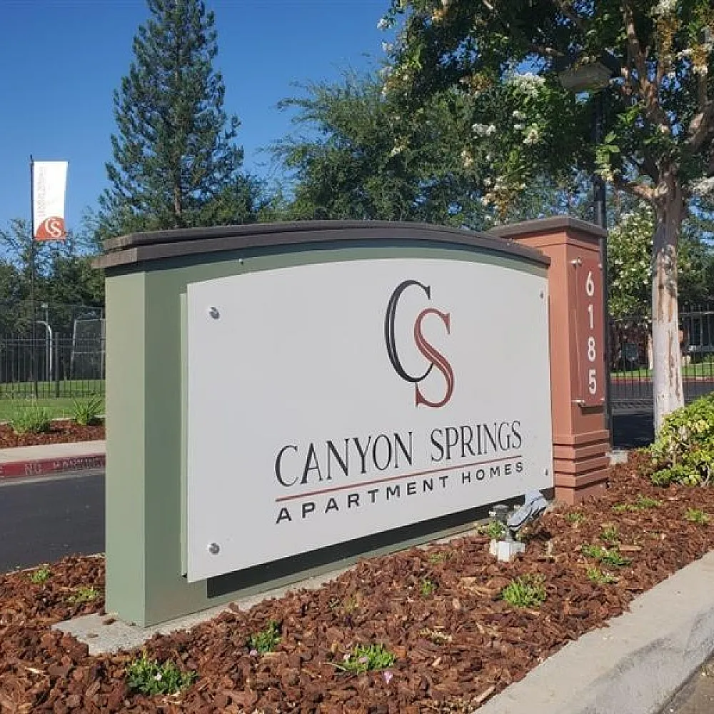 Inviting entrance sign for Canyon Springs Apartment Homes, set in lush green surroundings.