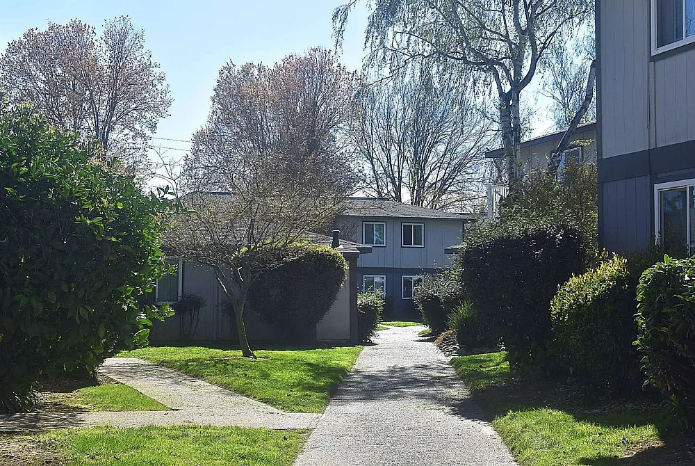 Charming apartment complex nestled among lush greenery and sunlit pathways, offering a serene living environment.