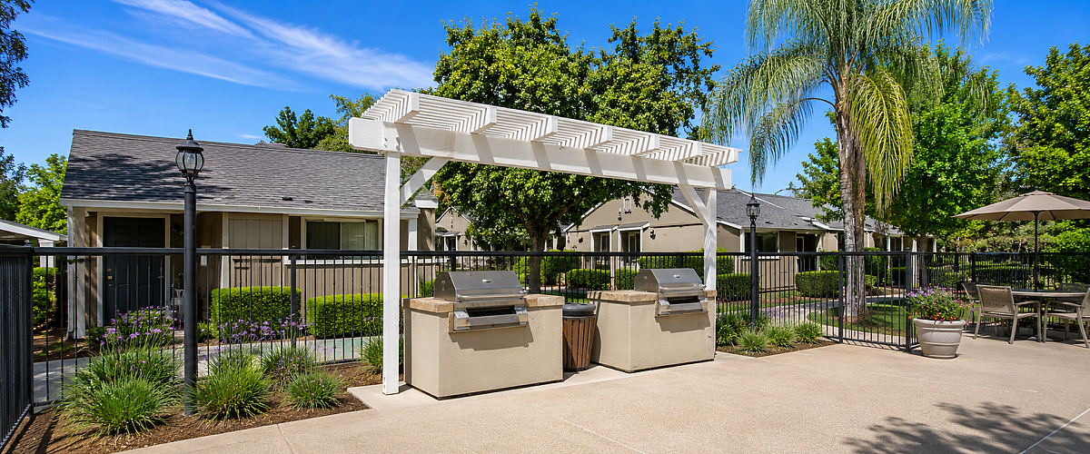 Inviting outdoor area with modern grilling station, shaded pergola, and lush greenery in a tranquil apartment community setting.