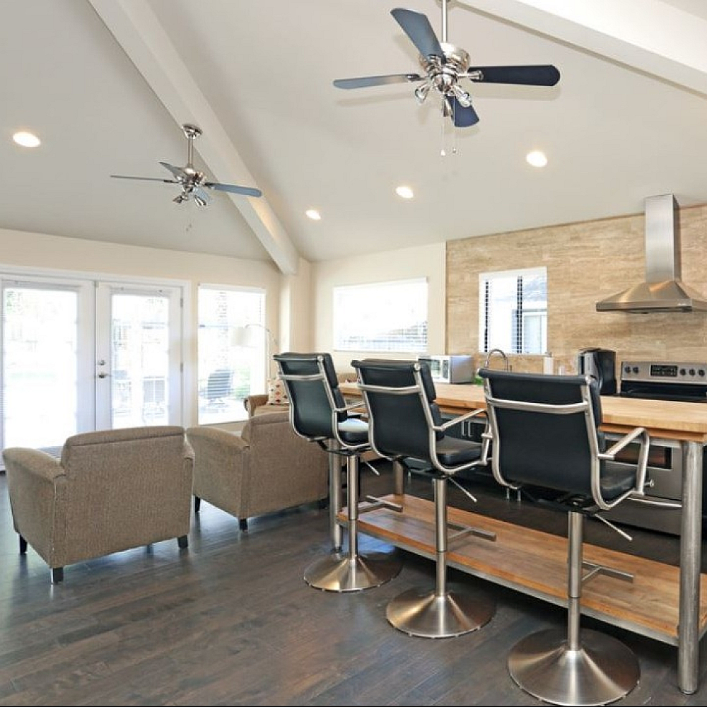 Modern kitchen and living area boasting sleek appliances, cozy seating, and stylish bar stools under high ceilings.