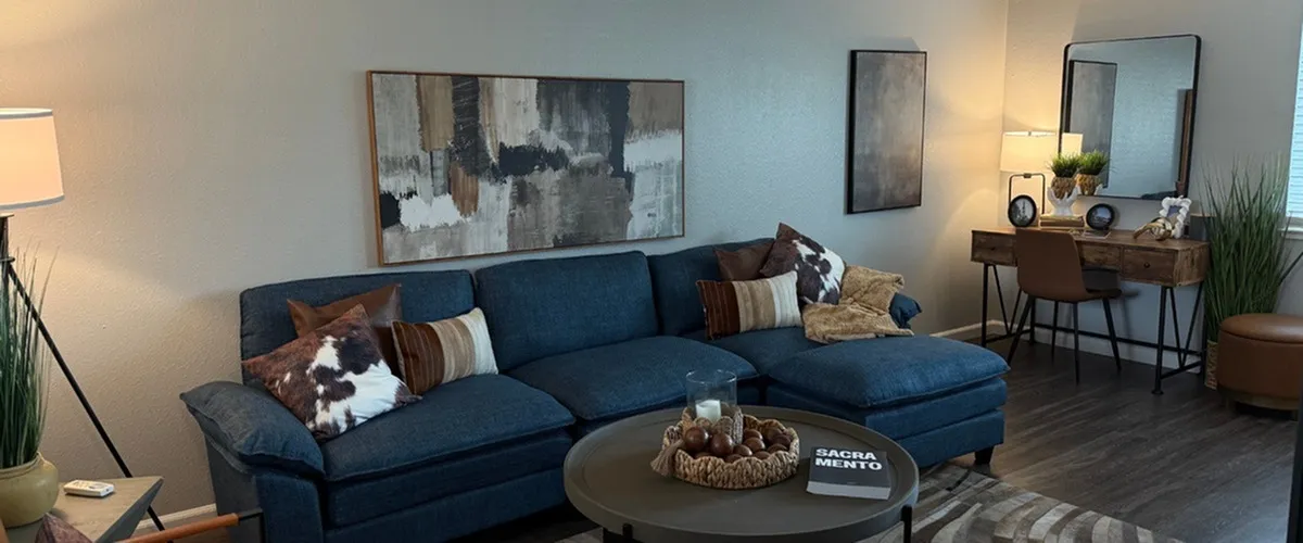 Chic living room with a cozy blue sectional sofa, stylish abstract art, and a modern work desk, accented by warm lighting and elegant decor.