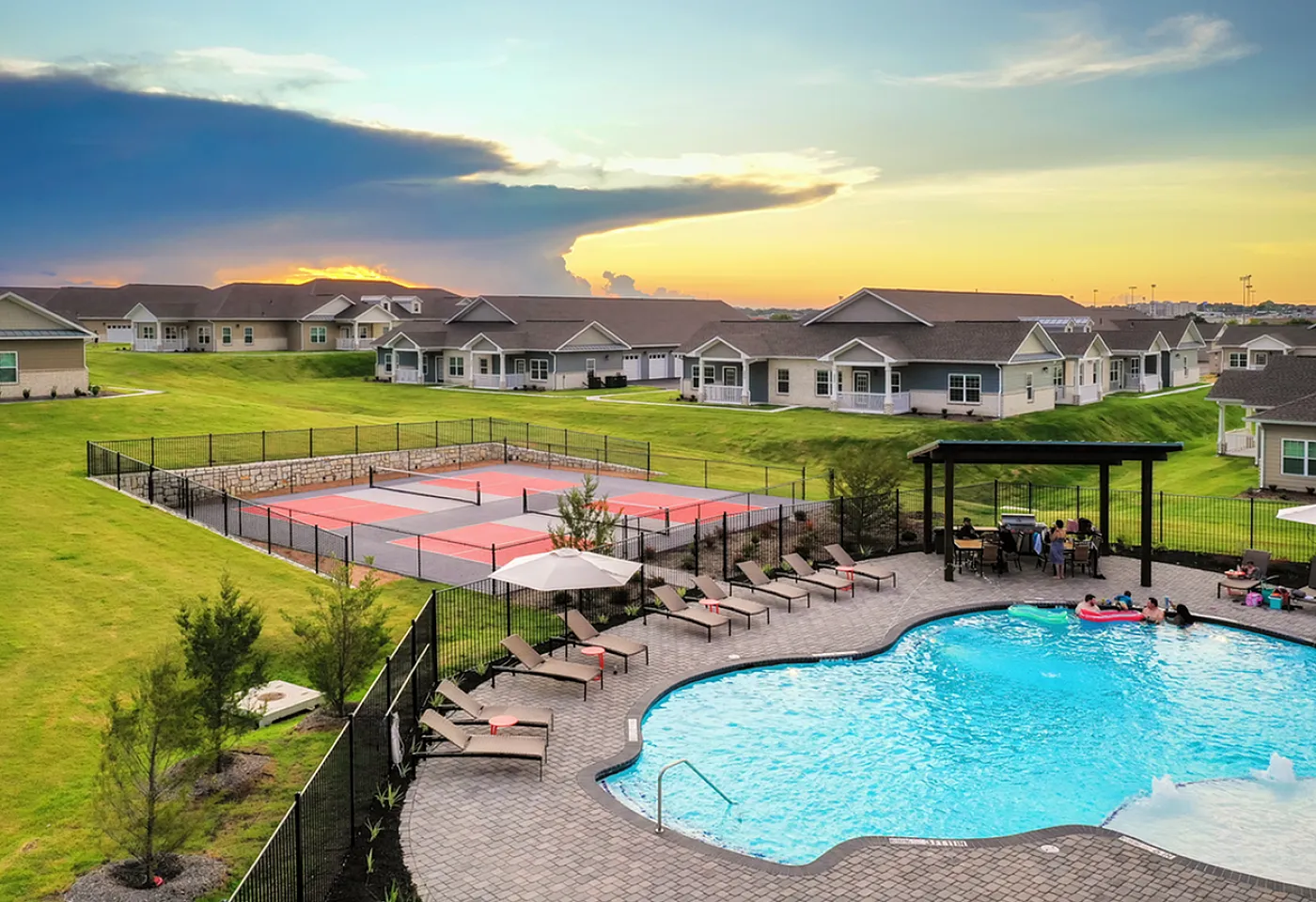 Charming residential community at sunset with modern homes, a vibrant tennis court, and a luxurious swimming pool for ultimate relaxation.