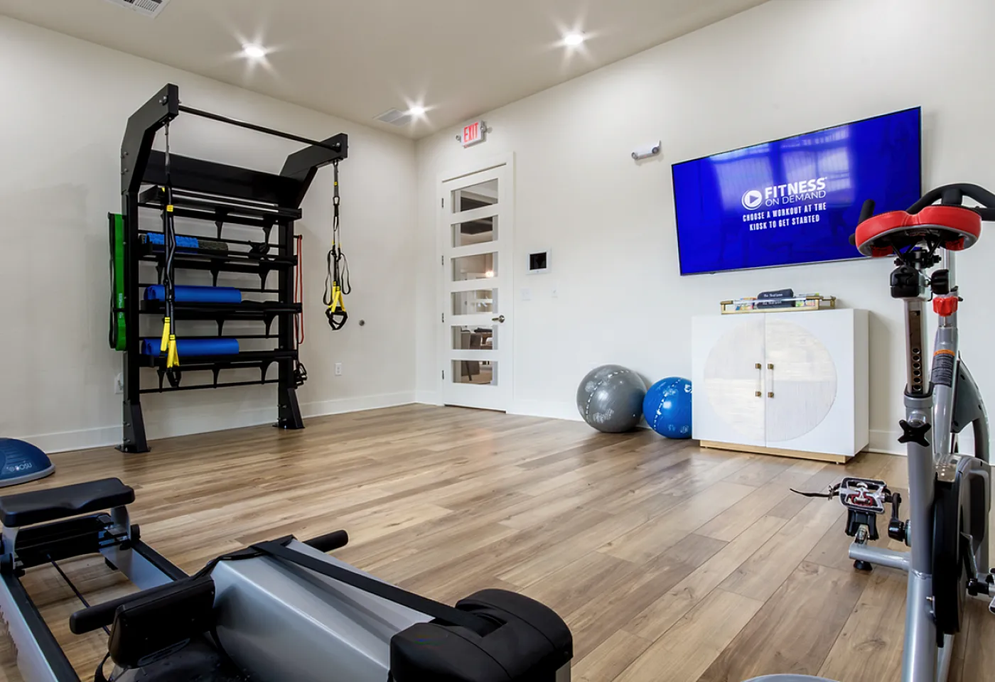 Modern home gym with sleek equipment including a rower and exercise bike, featuring bright wooden floors and a large screen for on-demand workouts.