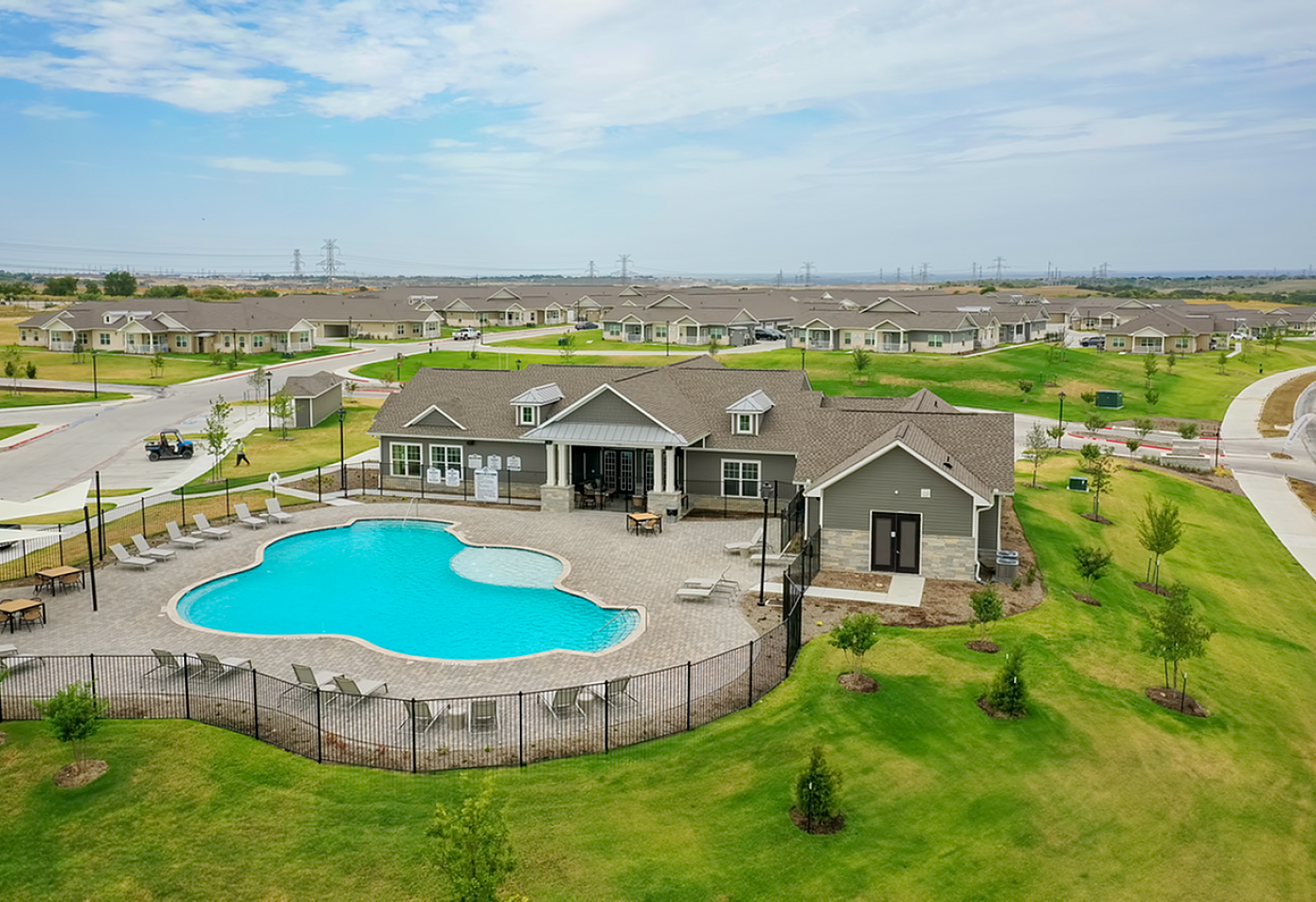 Expansive community view featuring a luxurious clubhouse with a sparkling pool, surrounded by beautifully manicured lawns and inviting walking paths.