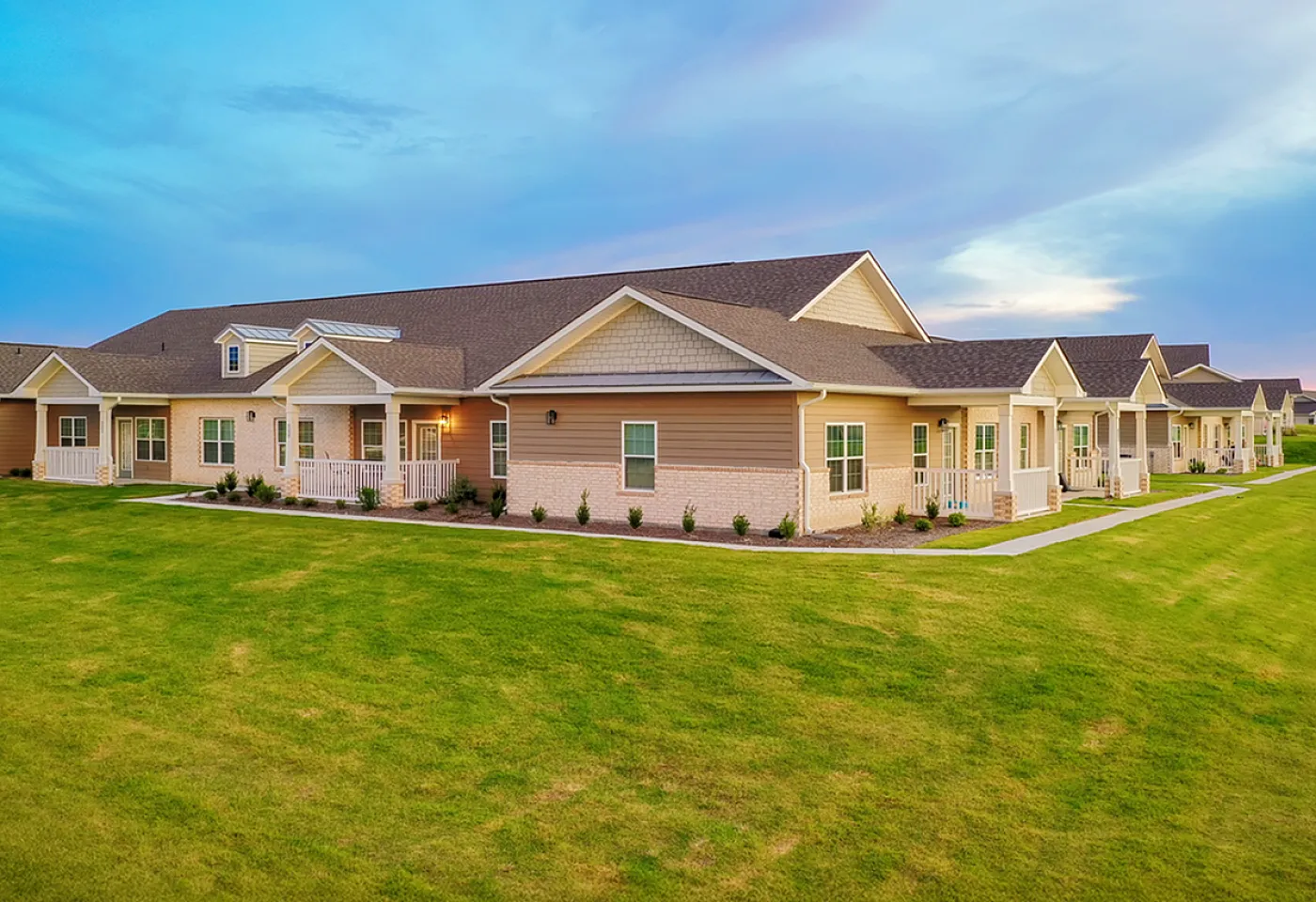Charming row of modern single-story homes with manicured lawns and inviting porches against a beautiful sky.