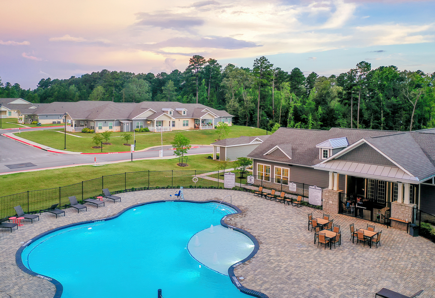 Stunning aerial view of modern living community featuring a sparkling pool, stylish deck area, and lush greenery, creating a serene and inviting atmosphere.
