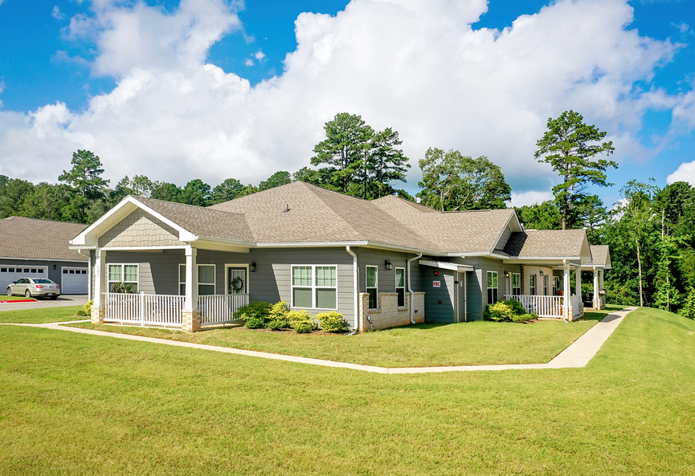 Charming gray bungalow surrounded by lush greenery with inviting front porch and clear blue sky backdrop.