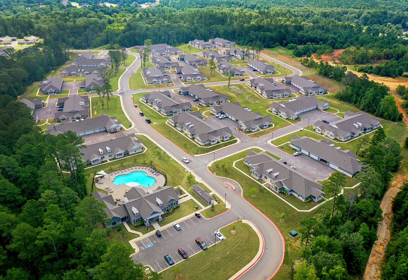 Aerial view of a luxurious residential community nestled within lush greenery, featuring spacious homes and a sparkling swimming pool.