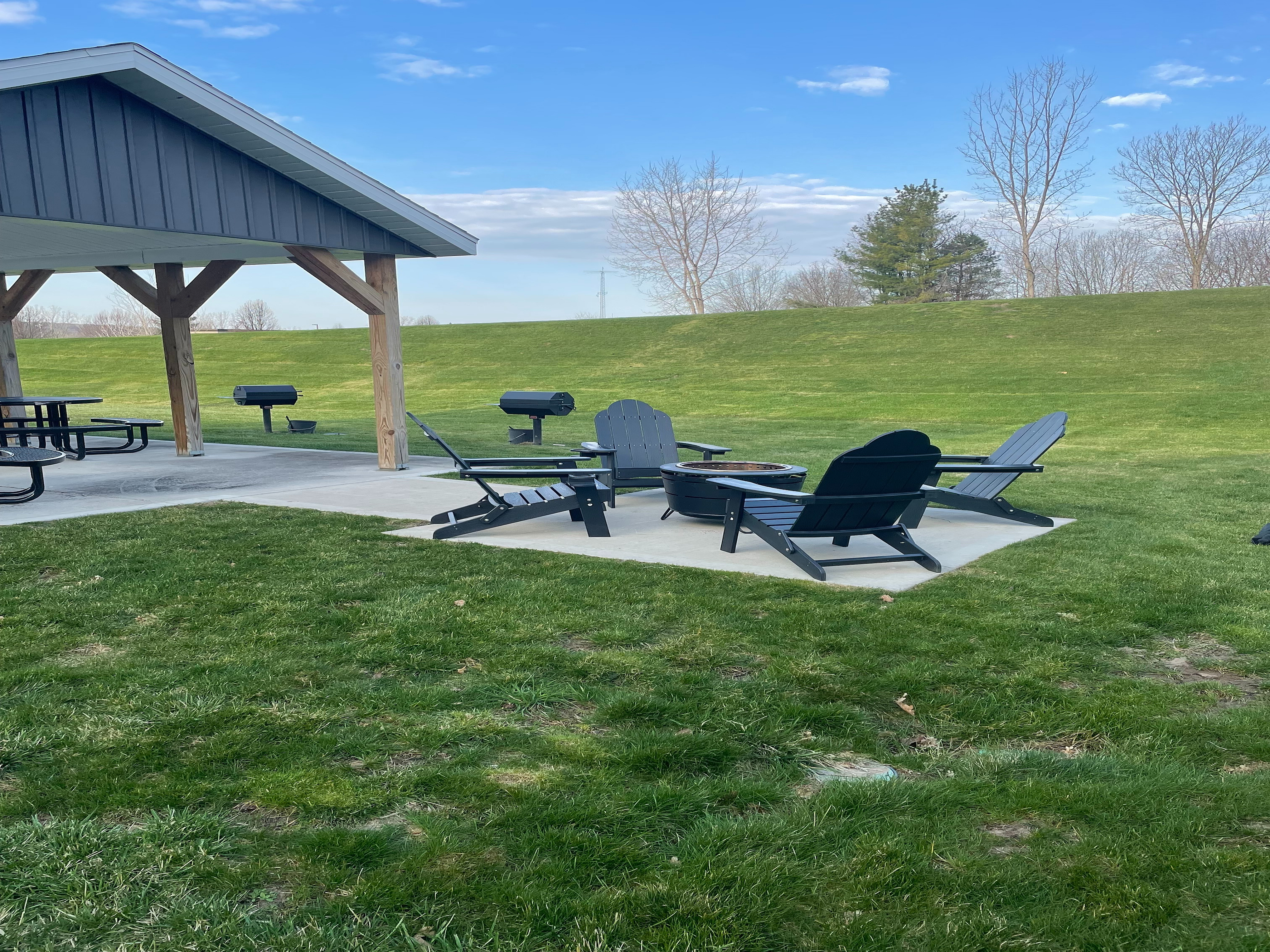 Charming outdoor area featuring Adirondack chairs, picnic tables, and grills under a picturesque sky, perfect for entertaining and relaxation.