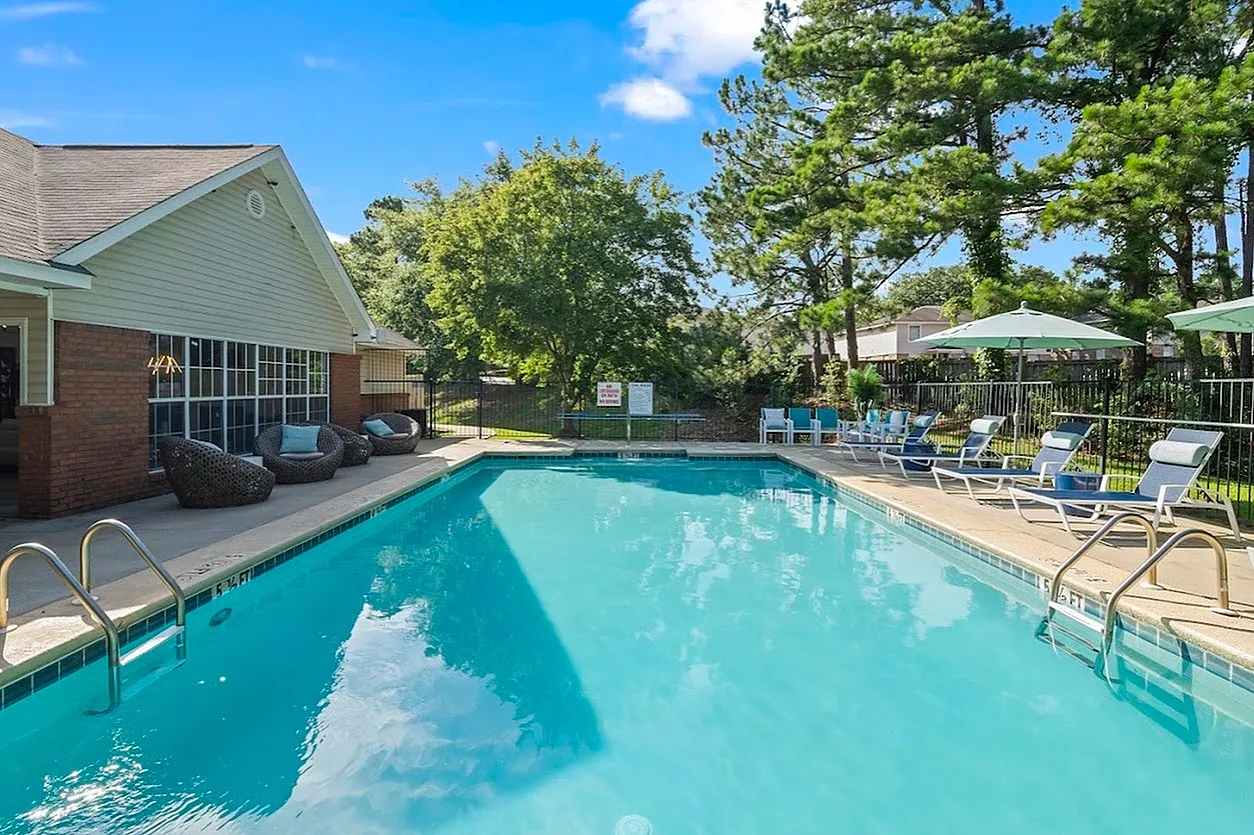 Inviting outdoor pool area with cozy loungers and lush greenery at a residential complex.