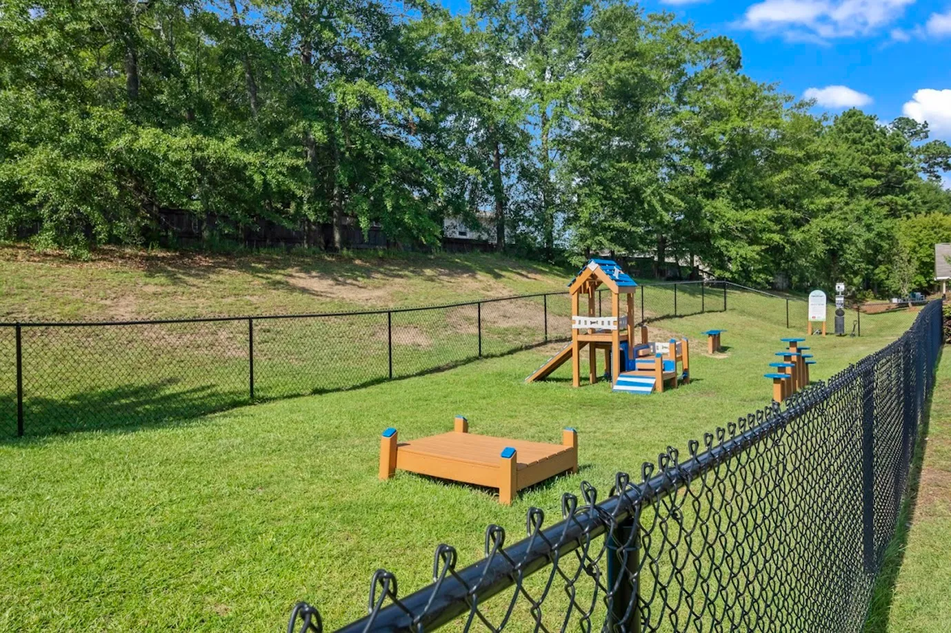 Inviting outdoor playground with play equipment, surrounded by lush greenery and a secure fence.