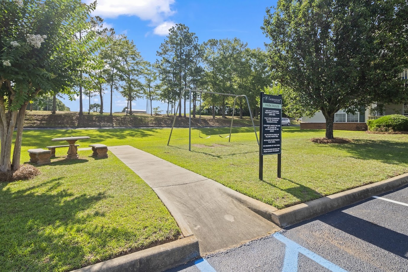 Serene outdoor area with swings, lush green grass, and benches under a bright sky.