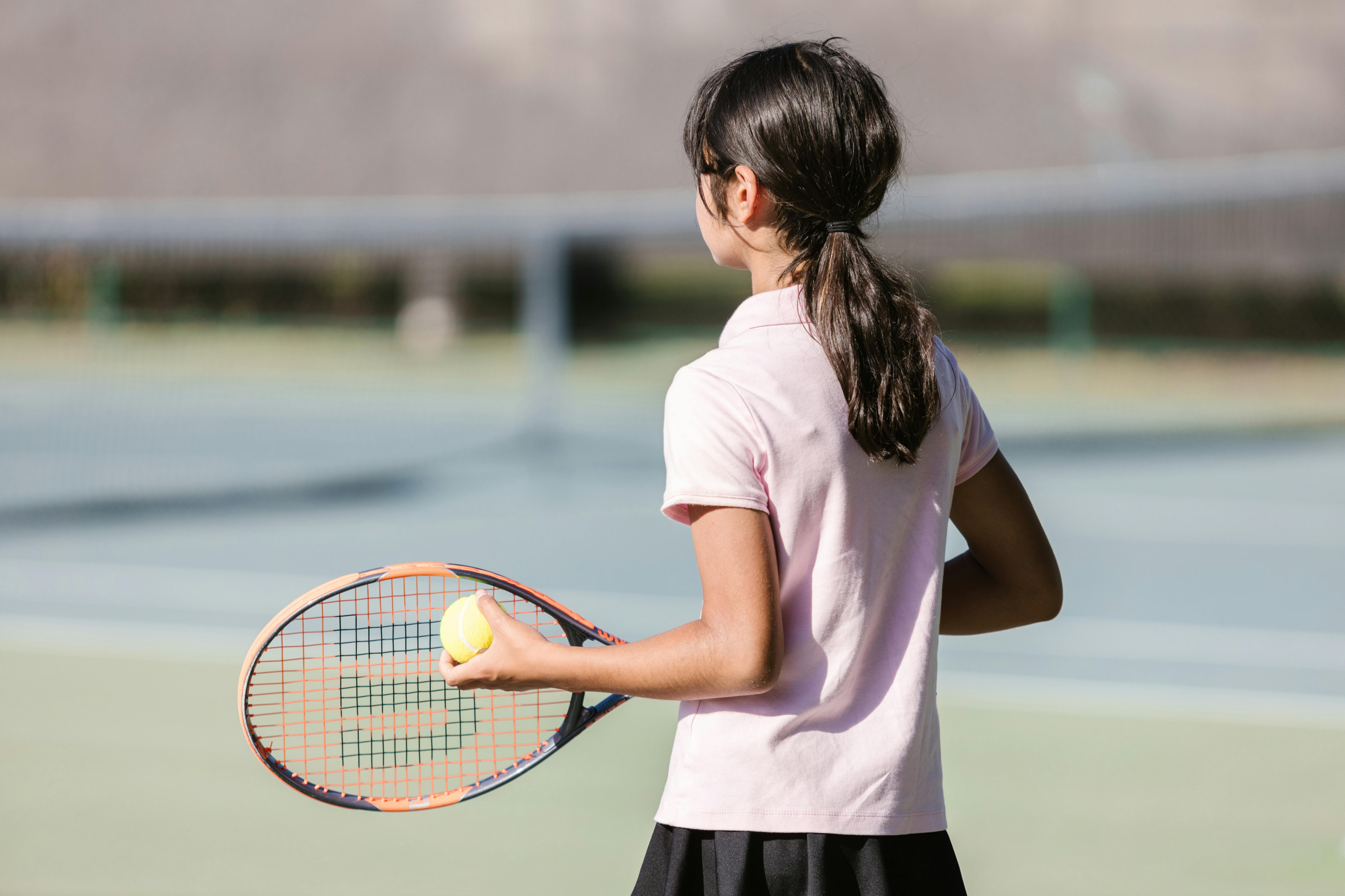Young tennis player in a pink shirt holding a racket and ball, ready for a match on the court.
