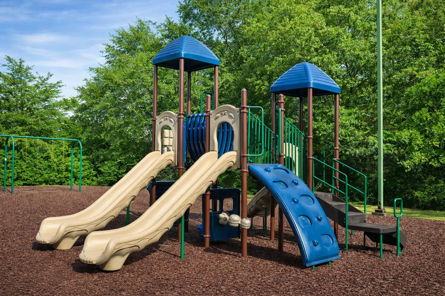 Vibrant playground with twin slides, climbing structures, and lush green surroundings, perfect for family fun.