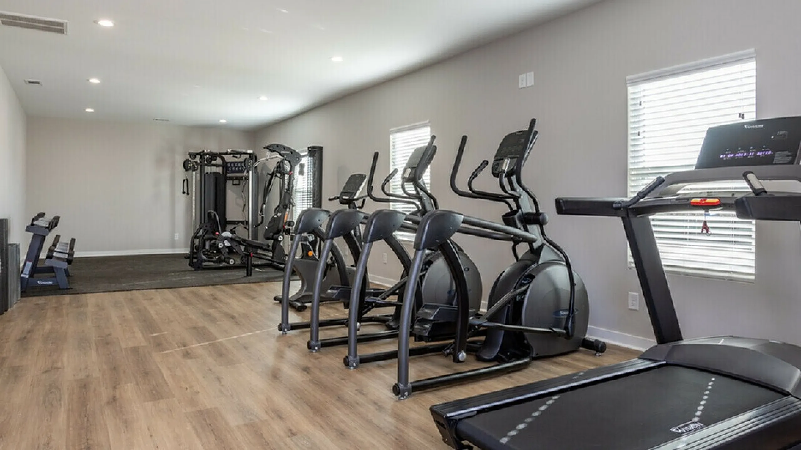 Spacious fitness center with elliptical machines, treadmill, and exercise equipment on wooden flooring.