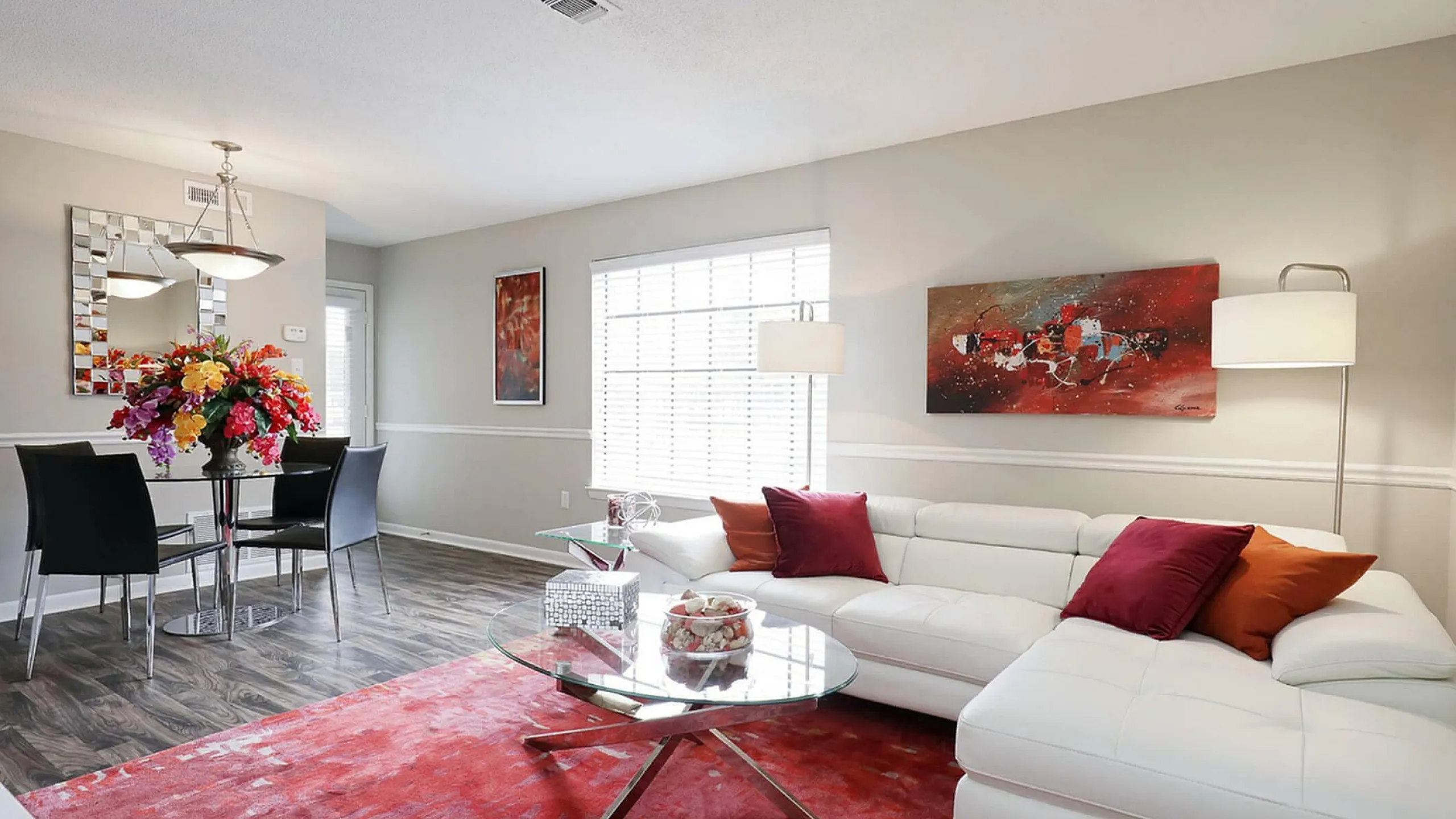 Bright, modern living room with sleek white sofa, vibrant red rug, and elegant dining area.