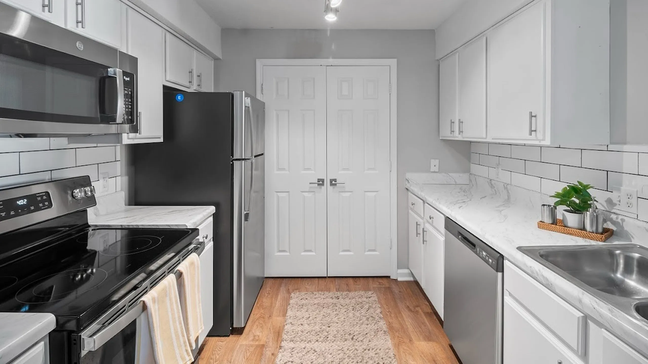Contemporary kitchen with stainless steel appliances, white cabinetry, and marble countertops.