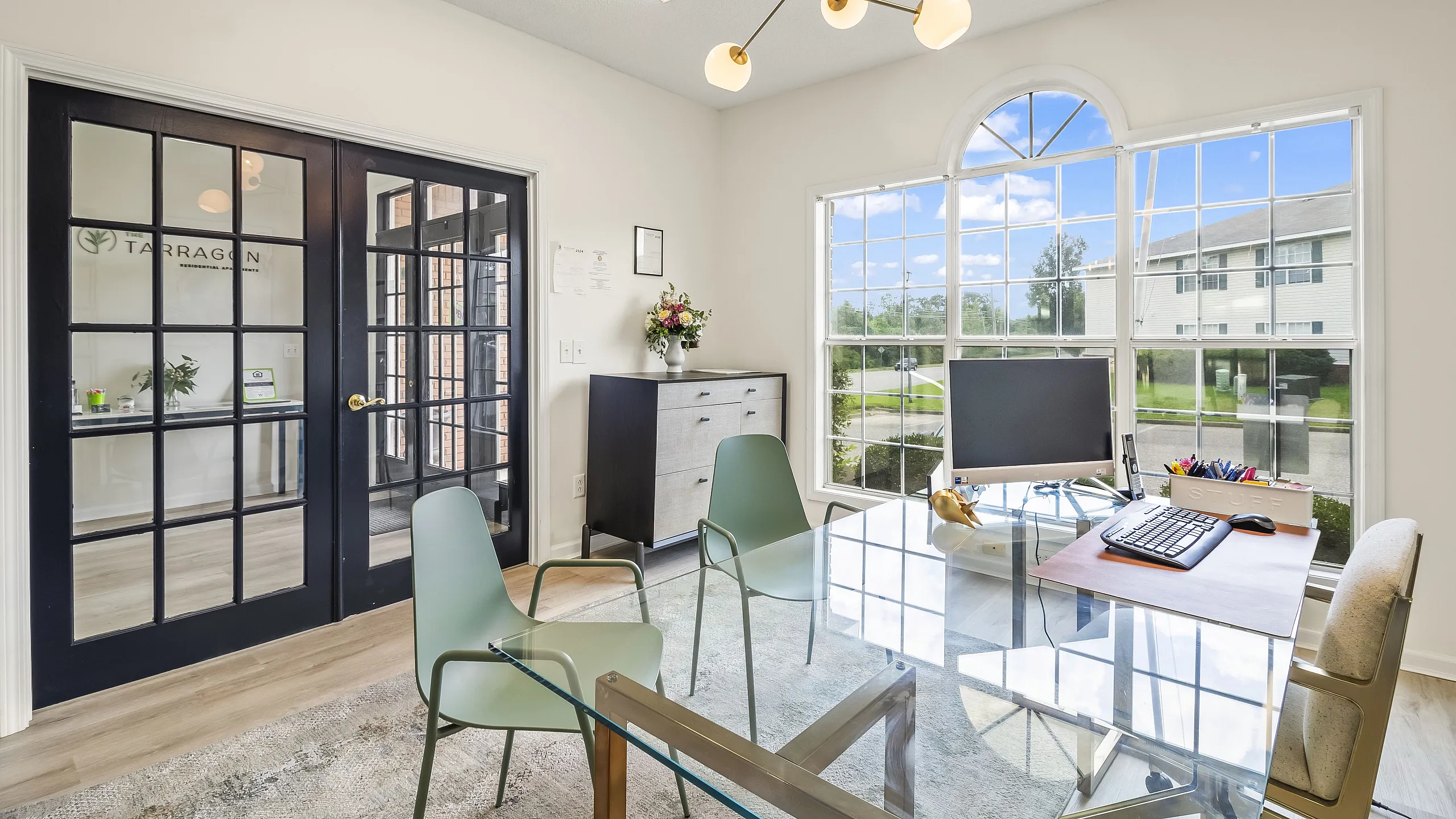 Modern office with glass desk, stylish chairs, and large window offering scenic views.