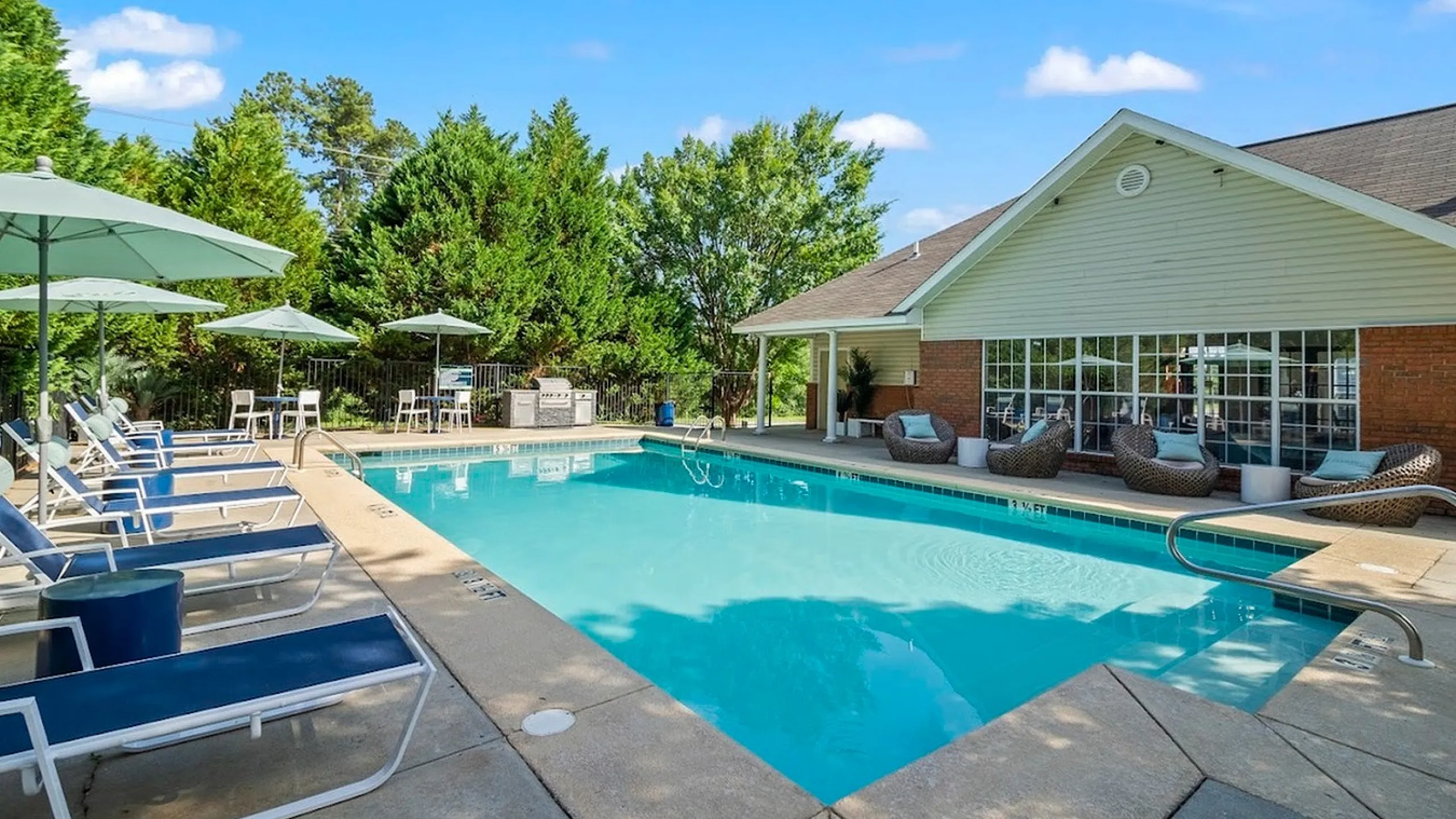 Inviting outdoor pool with lounge chairs and shaded seating, adjacent to a modern clubhouse.