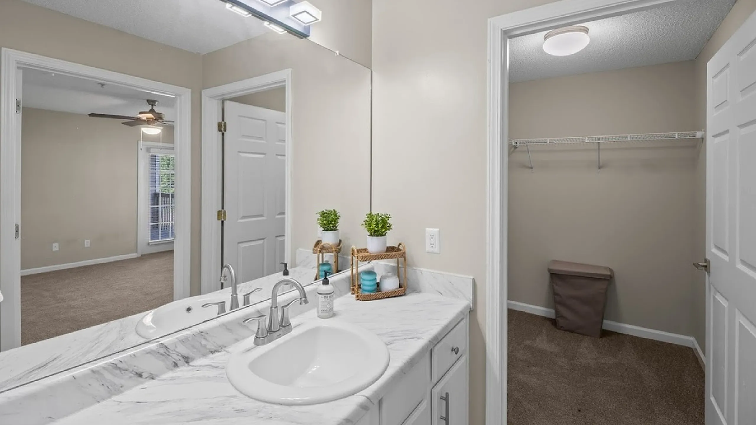 Modern bathroom featuring a marble countertop with dual sinks and access to a spacious walk-in closet.