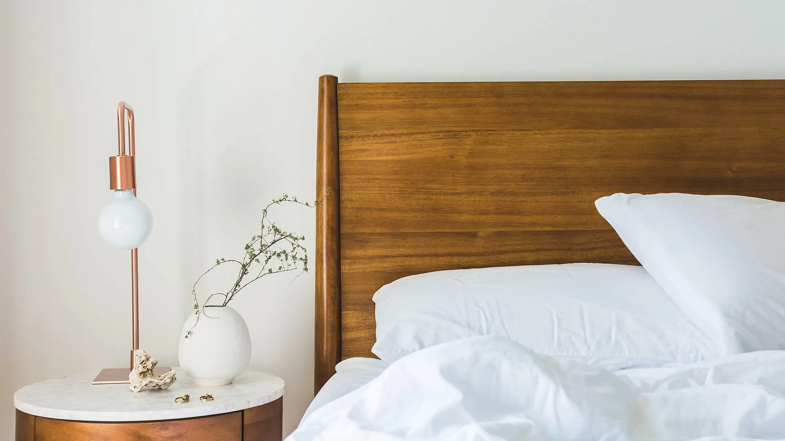 Inviting bedroom with a wooden headboard, crisp white bedding, and a stylish bedside table with a modern lamp.