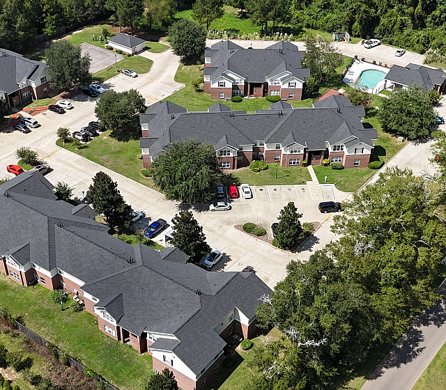 Aerial view of a beautifully landscaped apartment complex with multiple buildings, a pool, and tennis courts.