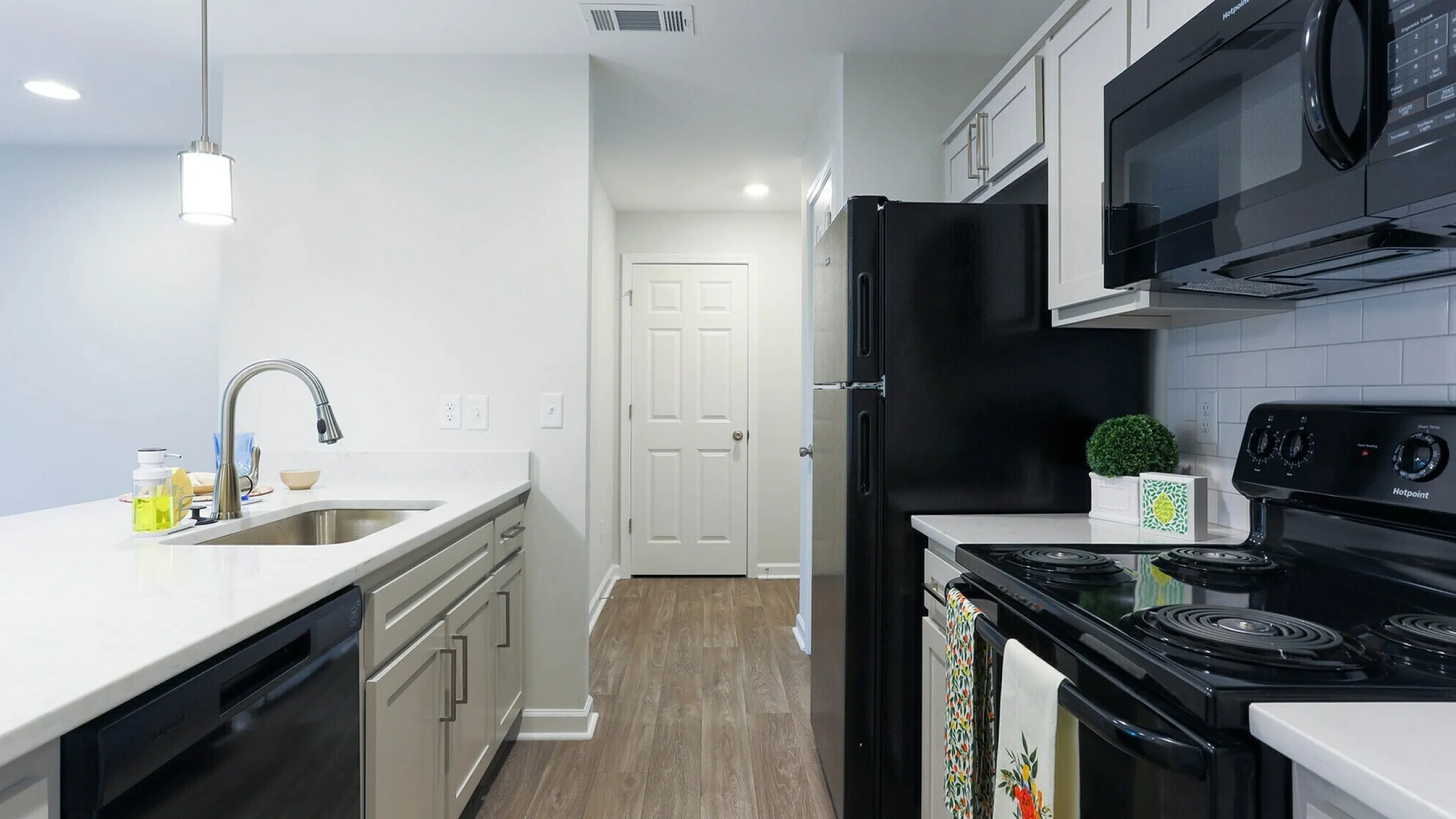 Contemporary kitchen with sleek black appliances, elegant white cabinets, and stylish pendant lighting over a spacious countertop.
