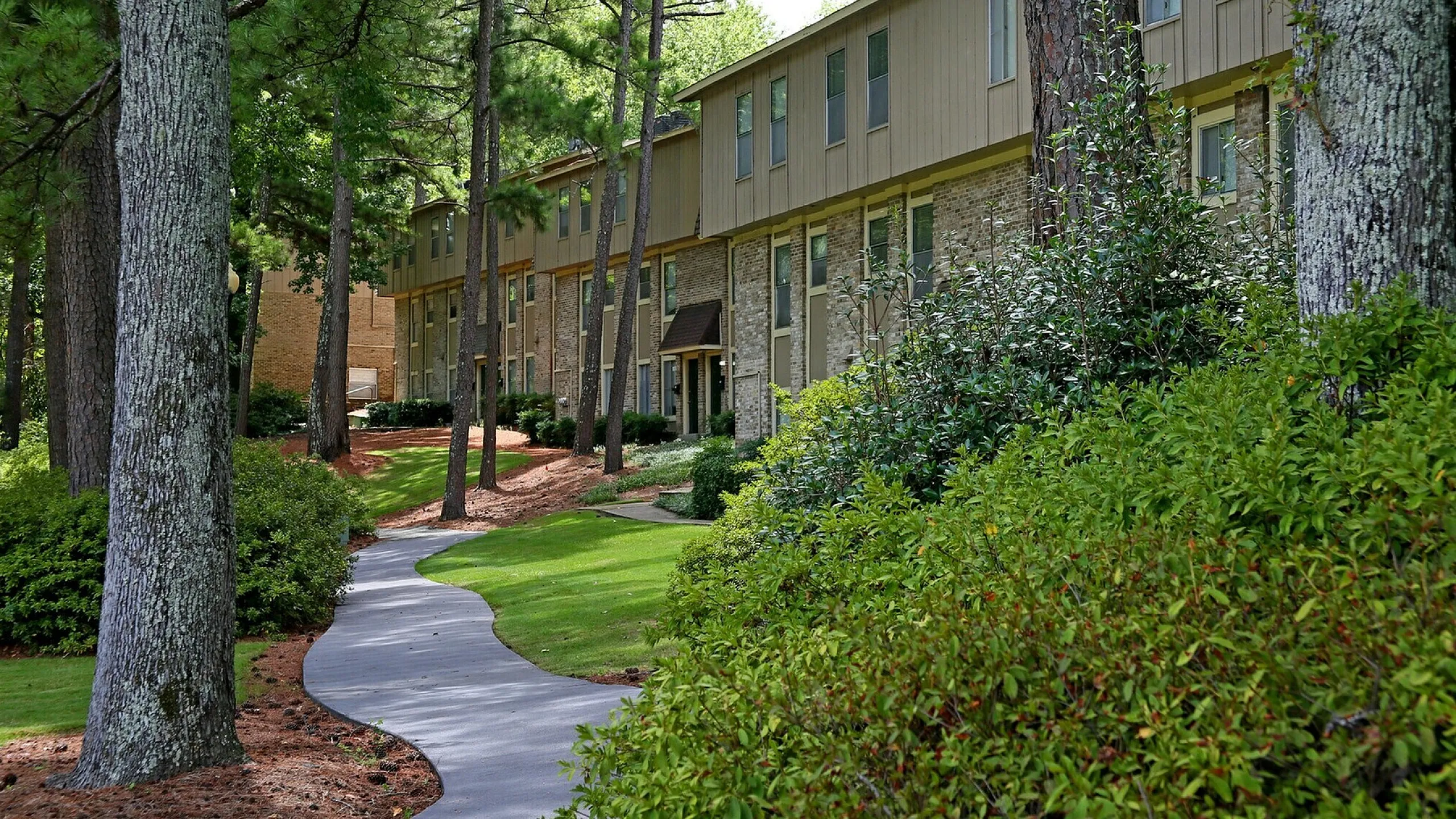 Charming apartment complex nestled among lush greenery with a scenic, winding pathway for a peaceful living environment.