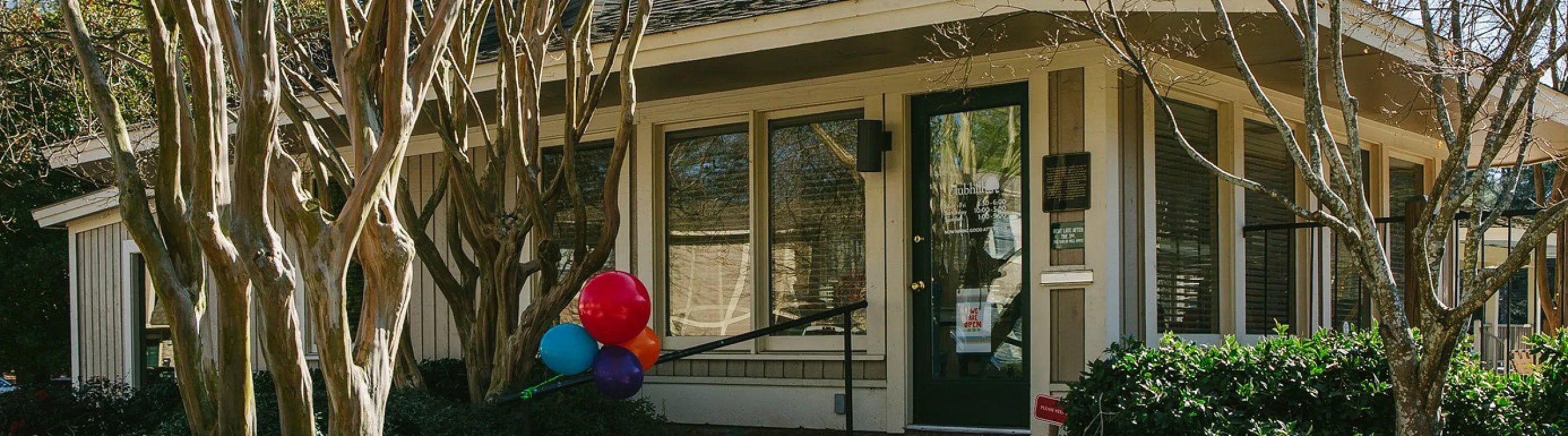 Charming suburban home surrounded by lush greenery, featuring a cozy entrance and vibrant balloons, nestled among mature trees in a serene neighborhood setting.
