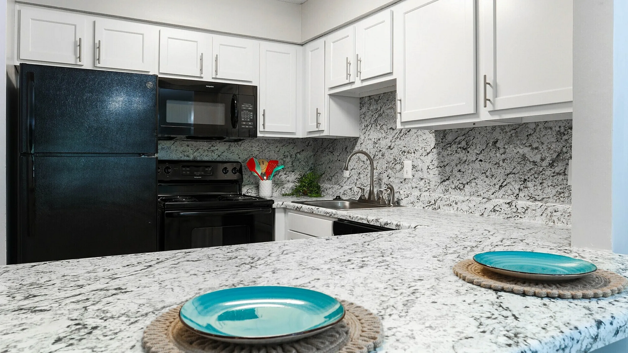 Modern kitchen with sleek black appliances, elegant white cabinetry, and stylish granite countertops, perfect for culinary enthusiasts.