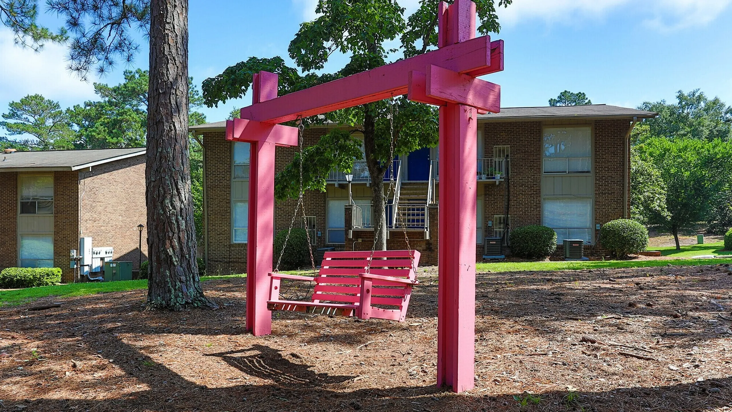 Charming pink swing set in a lush, green apartment complex. Perfect for relaxing in the serene outdoor space.