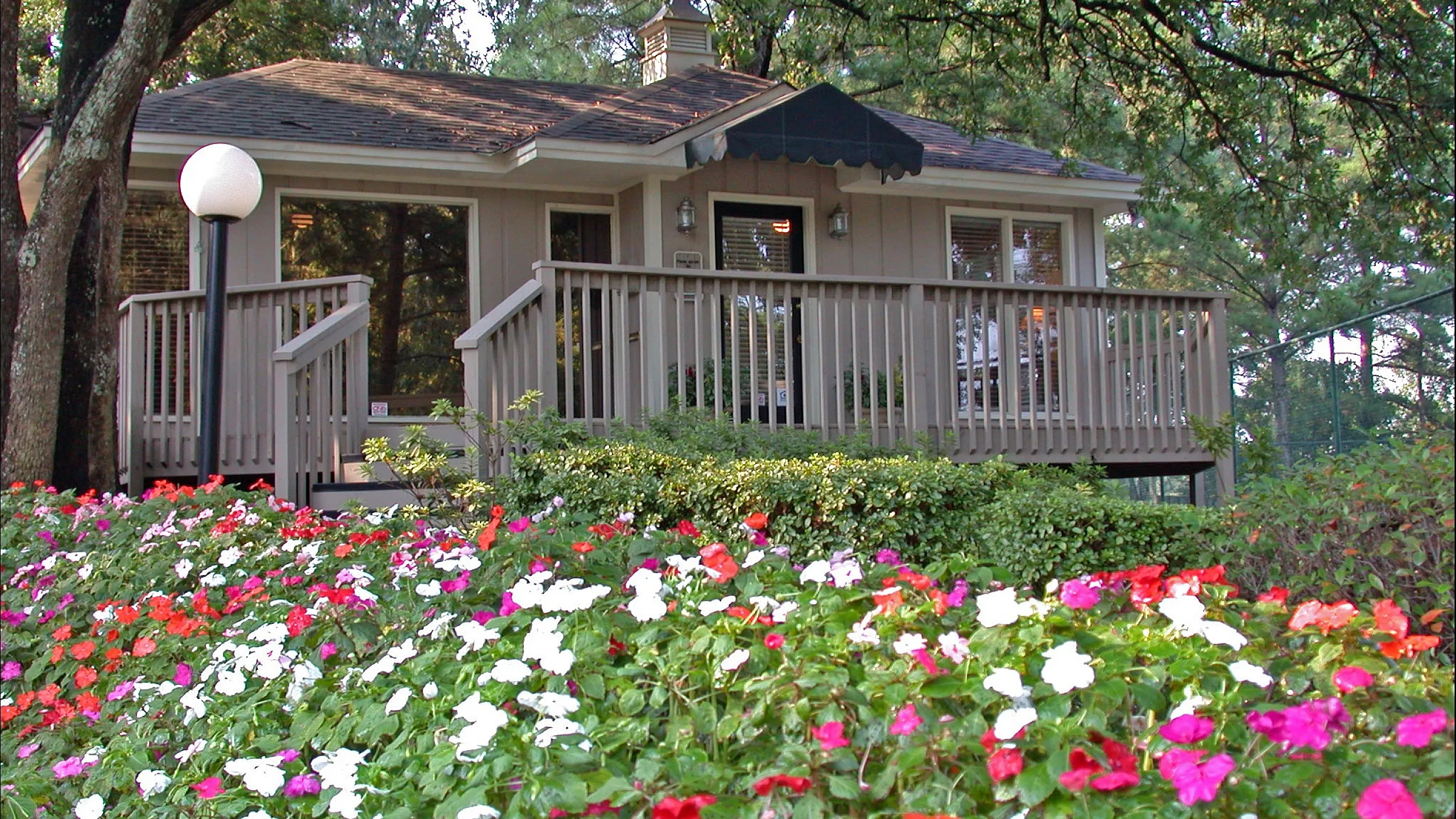 Charming cottage-style apartment with a spacious wooden deck, surrounded by vibrant flower gardens and lush greenery, perfect for a tranquil retreat.