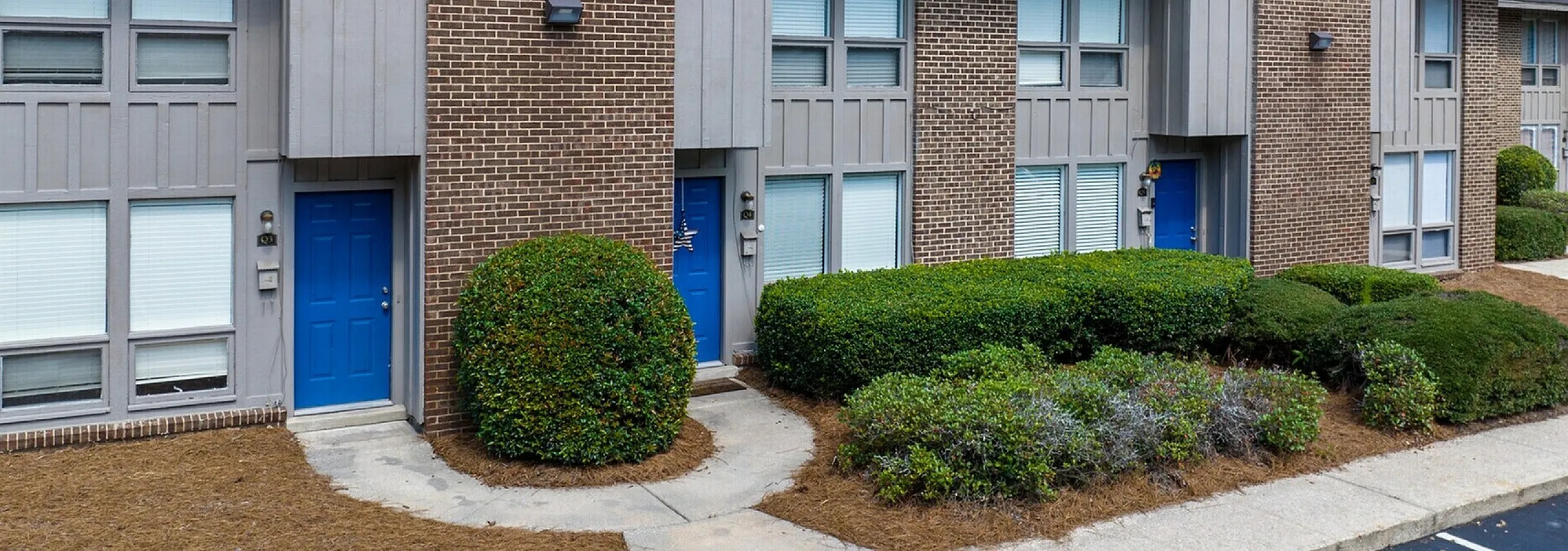 Charming townhouse with classic brick facade, vibrant blue doors, and lush greenery, perfect for comfortable suburban living.