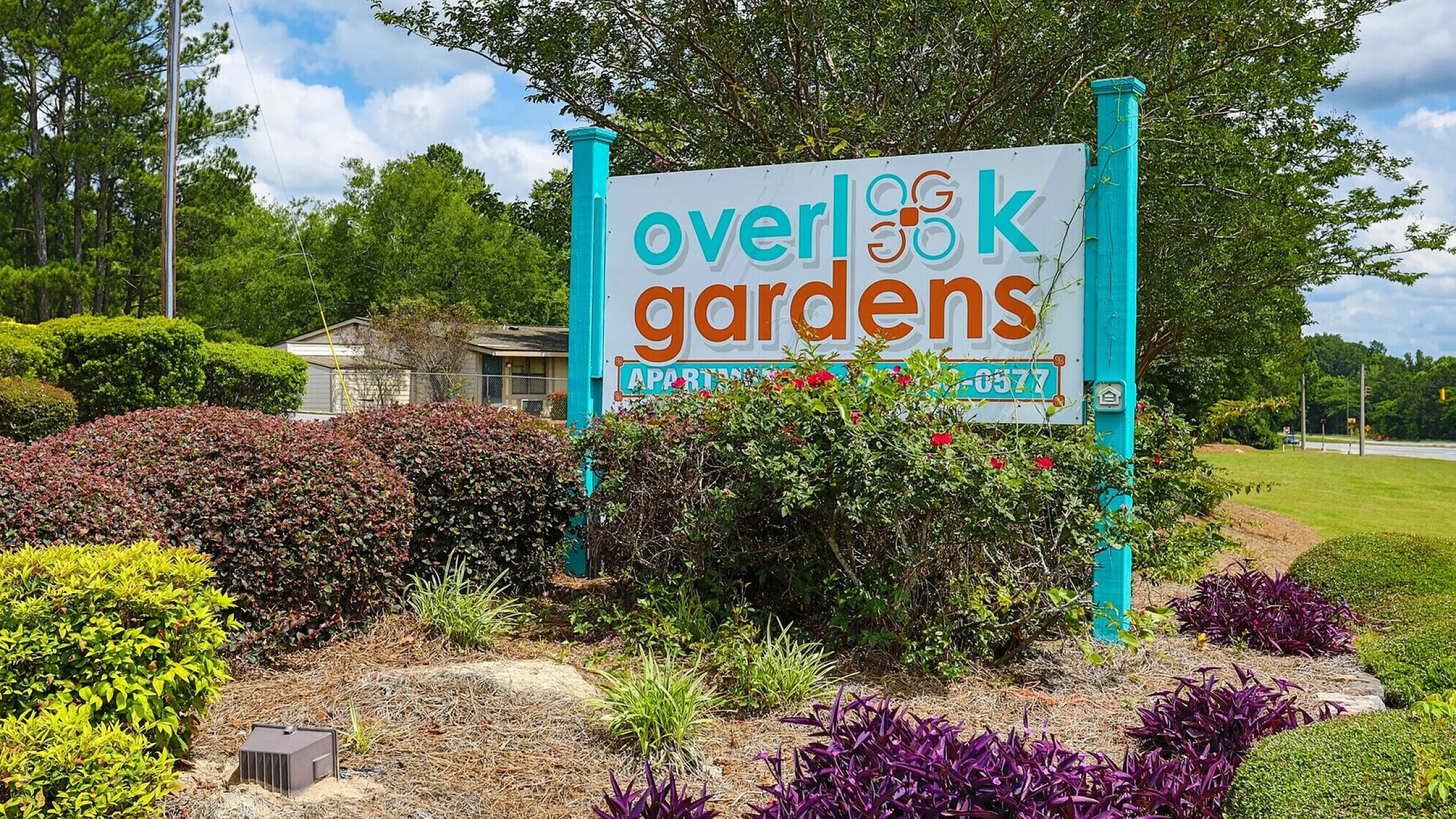 Inviting entrance sign for Overlook Gardens Apartments, surrounded by lush greenery and vibrant flowers.