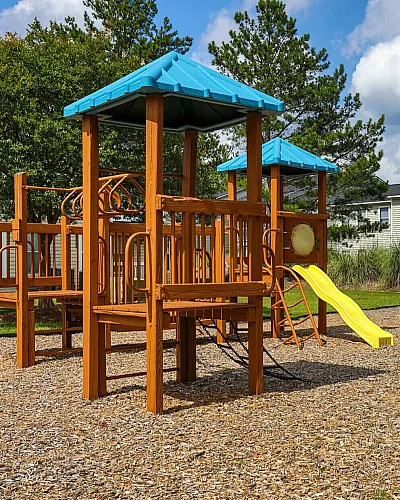 Charming apartment community with vibrant playground featuring slides and swings, surrounded by lush greenery.