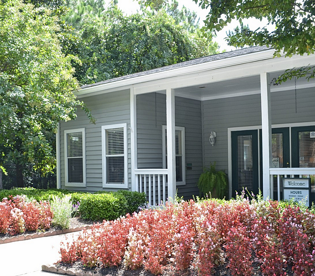 Charming apartment entrance with a welcoming porch, lush greenery, and vibrant flower beds, perfect for a serene living environment.
