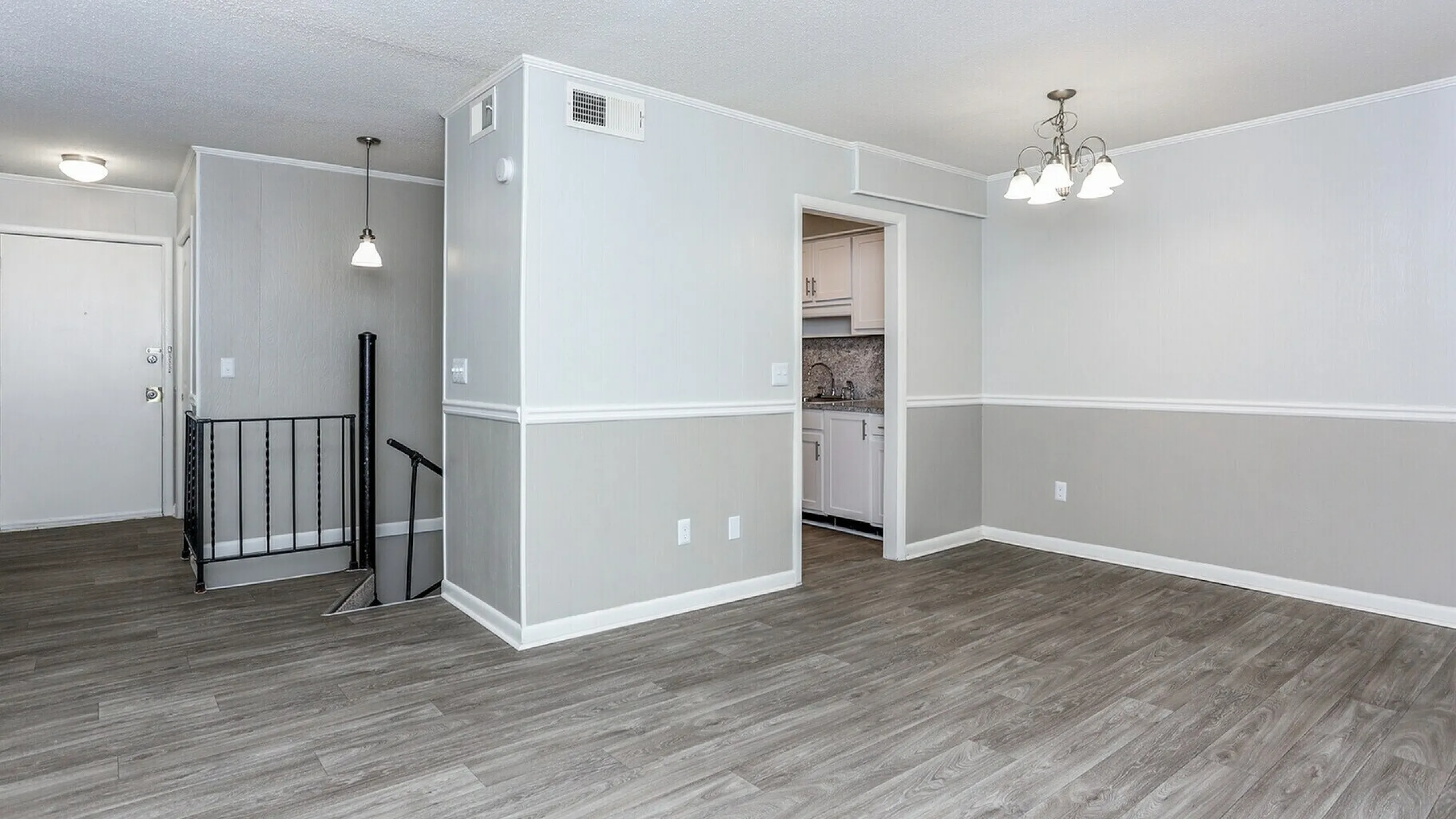 Modern open-concept apartment with wood-look flooring, bright lighting, and access to a sleek kitchen through an inviting hallway.