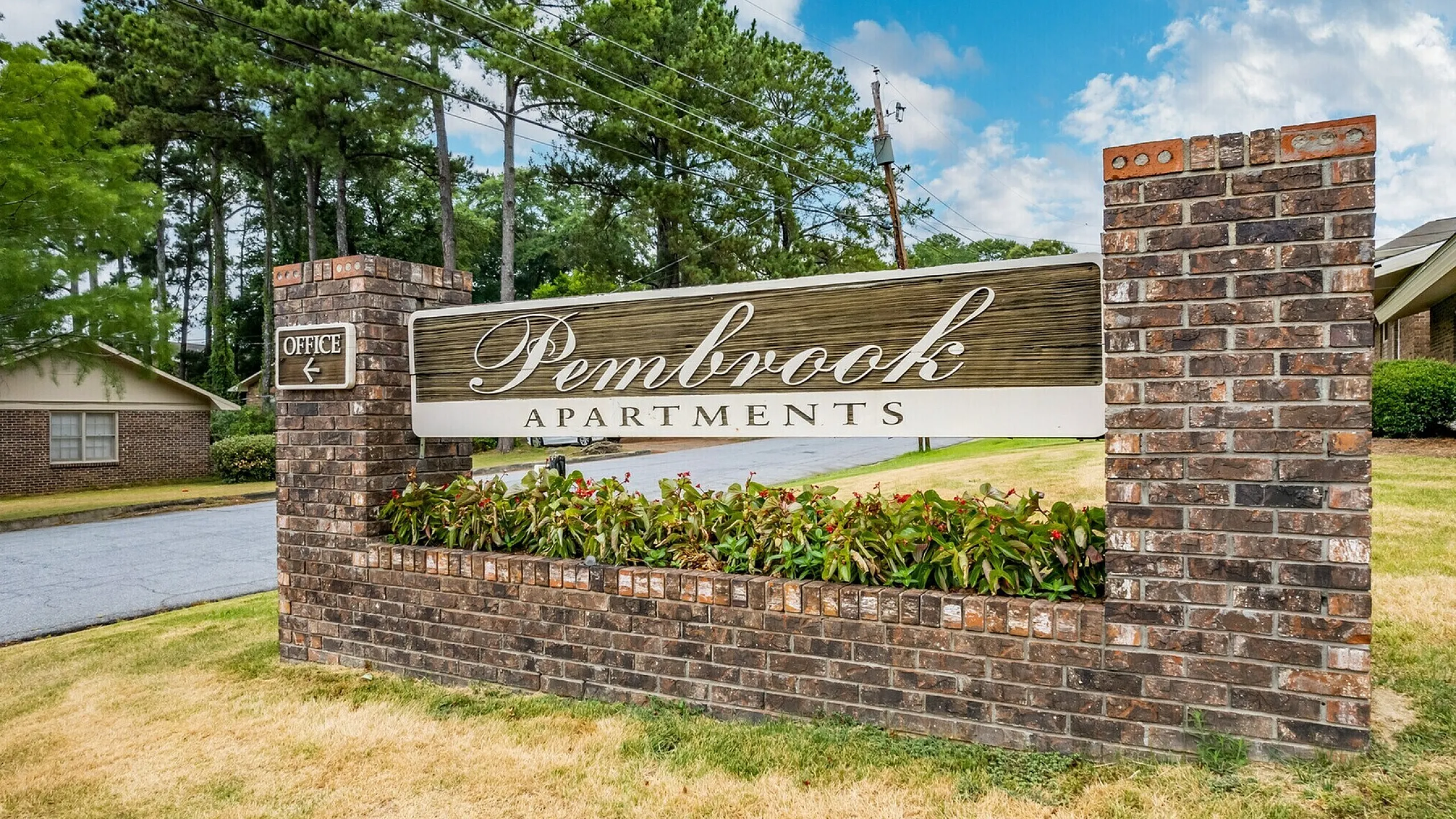 Charming Pembrook Apartments entrance sign surrounded by lush greenery, inviting atmosphere, and brick pillars under a clear blue sky.