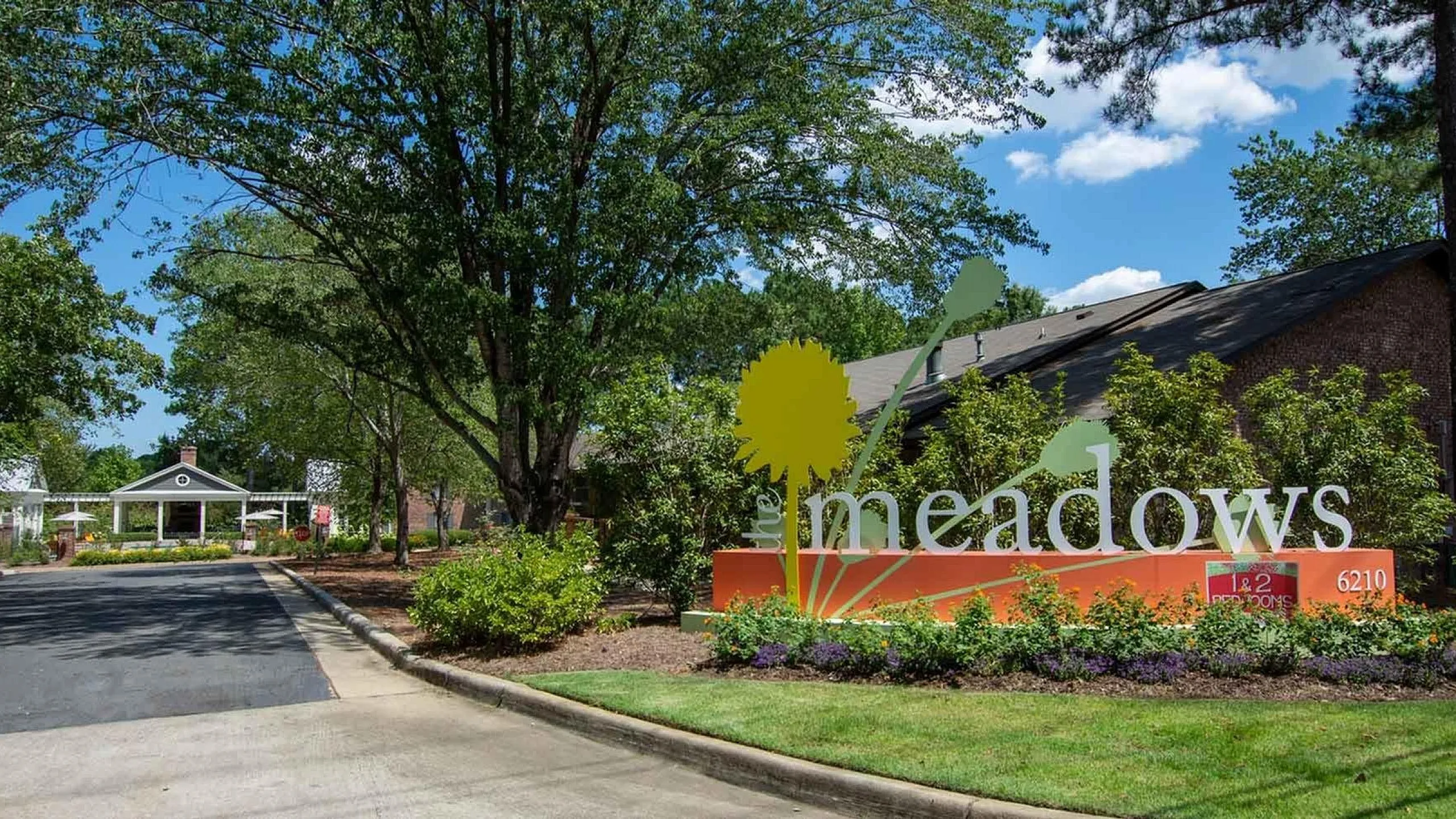 Charming apartment community entrance with lush greenery and vibrant signage at The Meadows, offering 1 and 2 bedroom options.