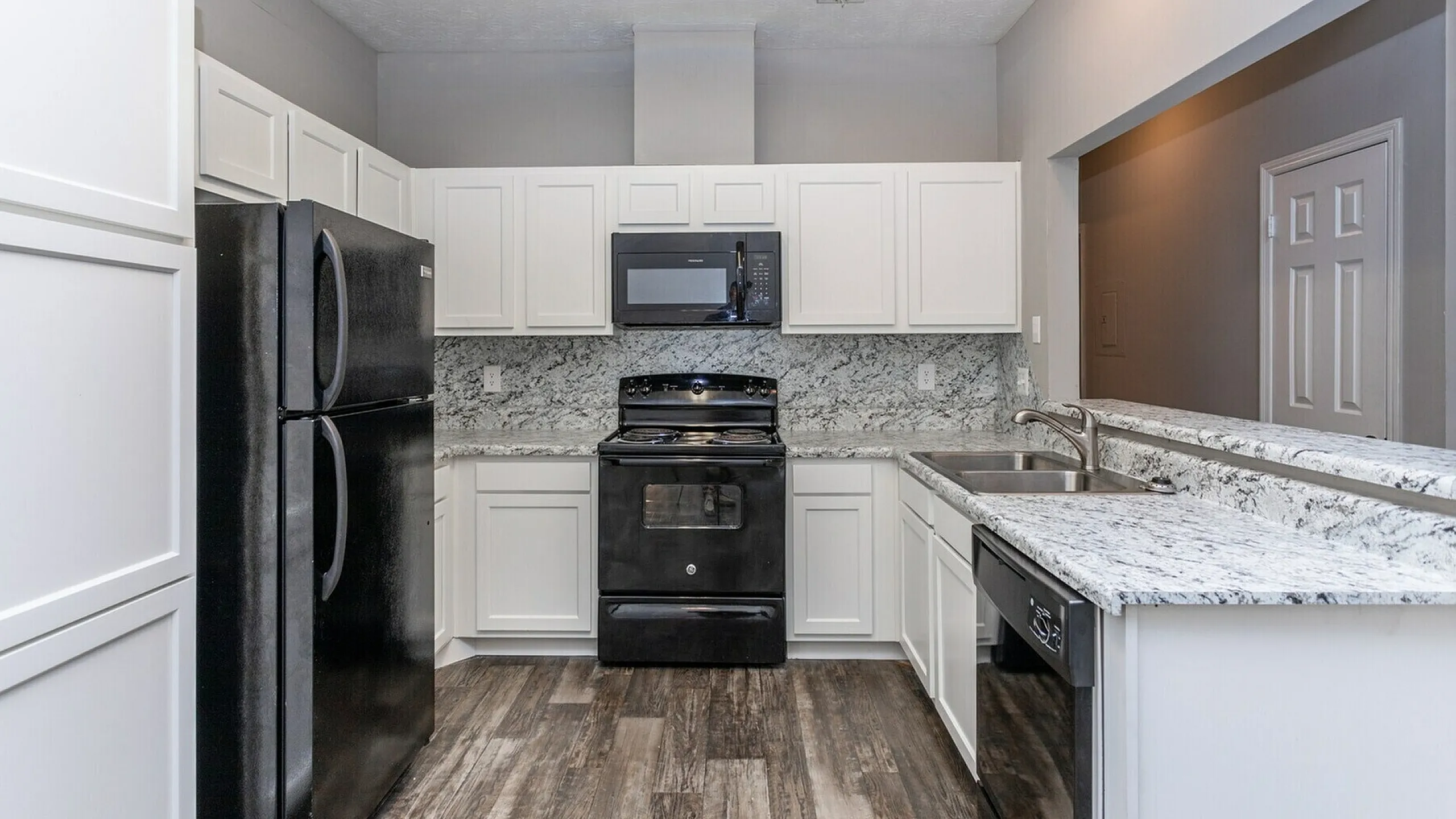 Modern kitchen featuring sleek black appliances, elegant white cabinetry, and stylish granite countertops with ample space.