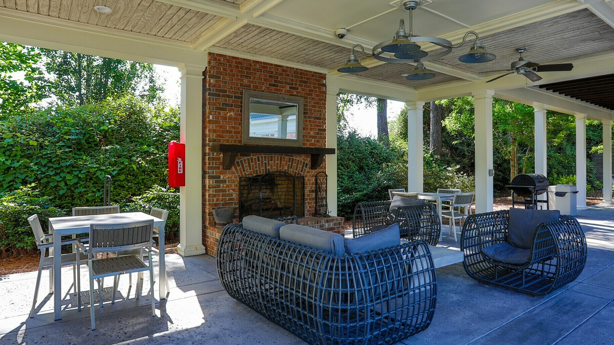 Inviting outdoor lounge area with modern wicker furniture, a cozy fireplace, and lush green surroundings, perfect for relaxation and entertaining.