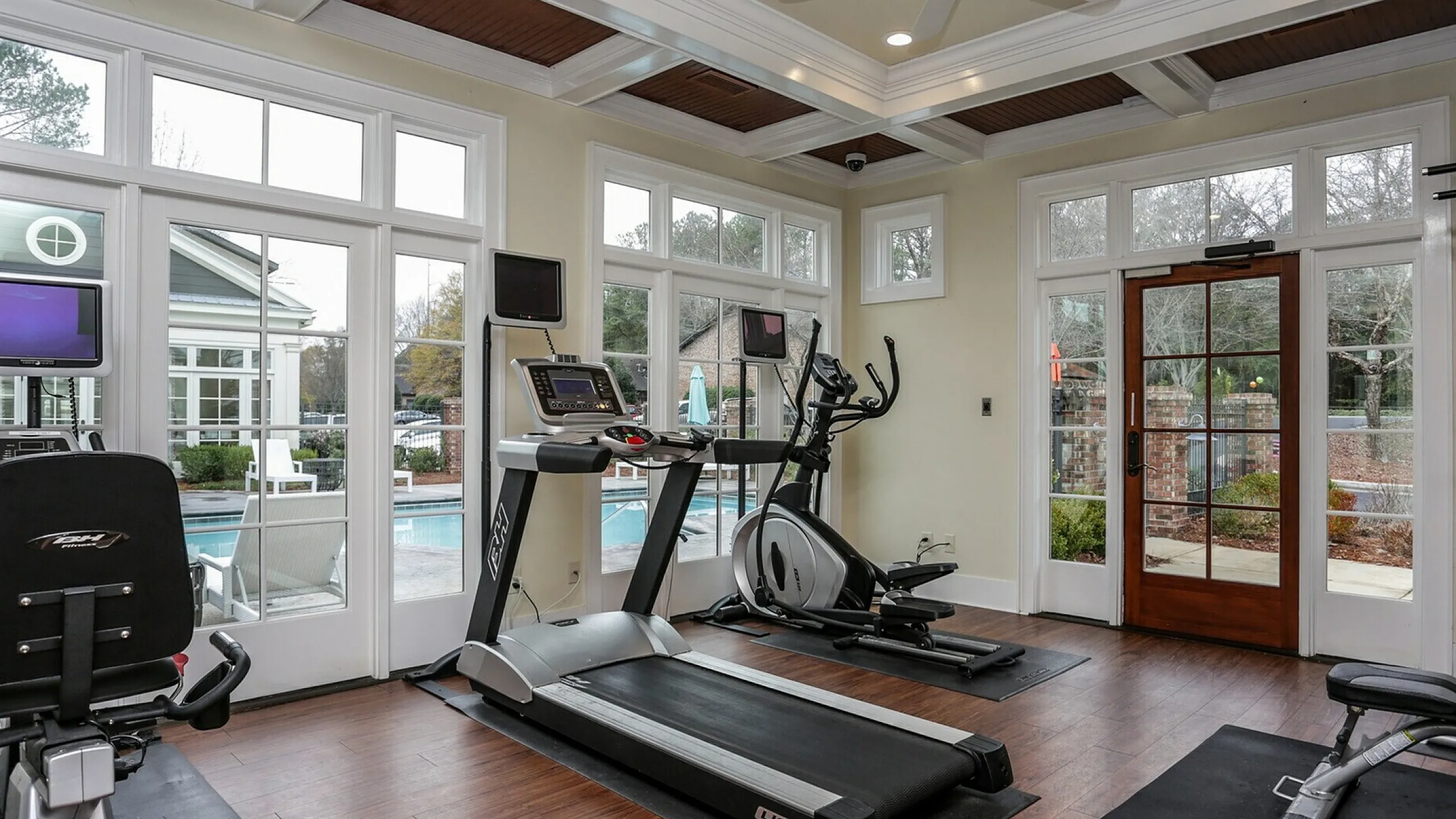 Modern fitness center with cardio and exercise equipment, featuring scenic views of a pristine outdoor pool through large windows.